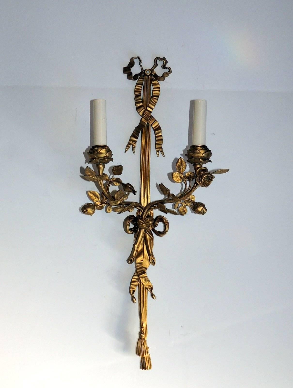 Wonderful pair of French doré bronze two-arm sconces. Beautiful ribbon top and draping down to the tassel at the bottom, each arm is a rose candle cup with floral and leaves surrounding them. 

Sold as a pair.

Measures: 22" L x 9" W x 4.5