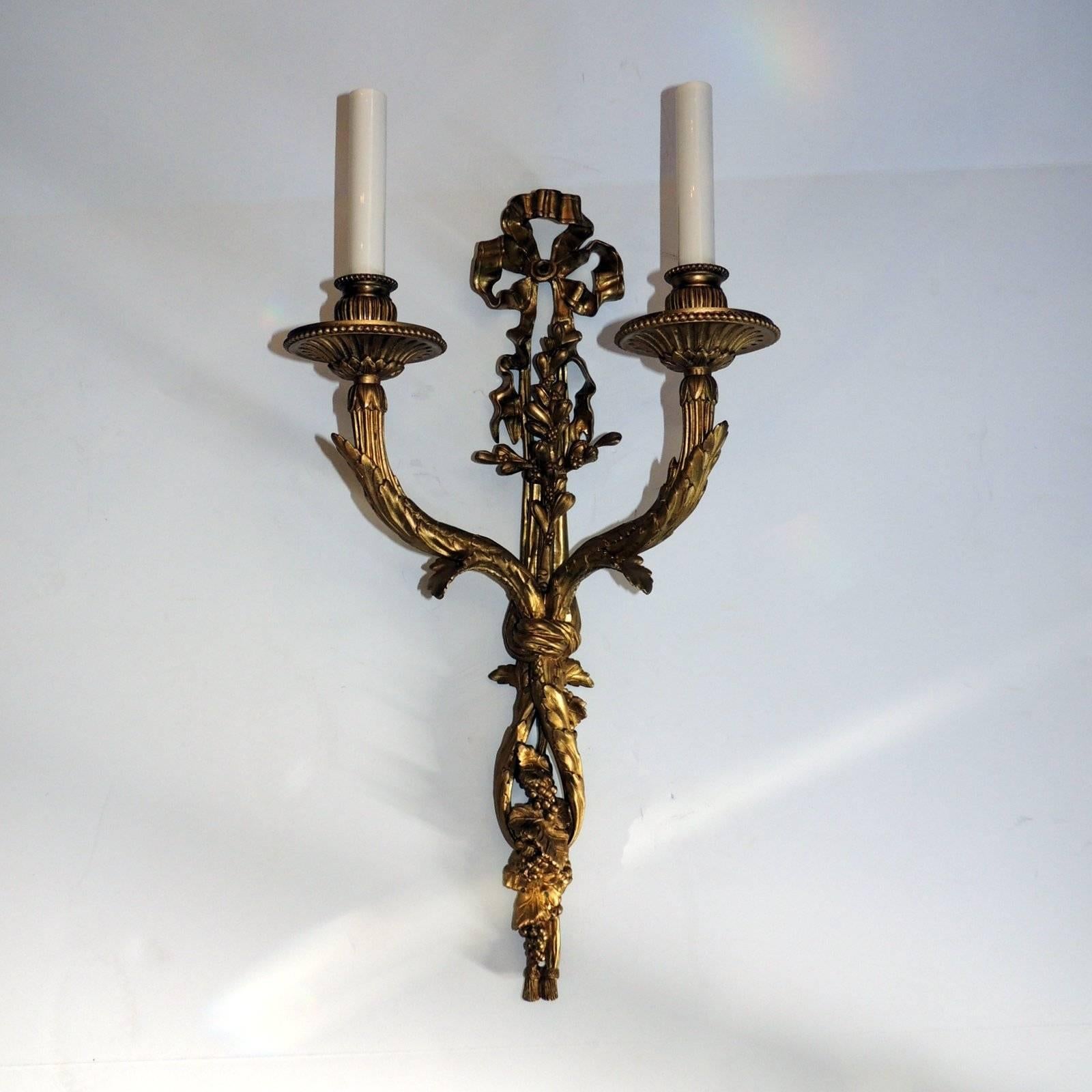 Incredibili dettagli sulla coppia di appliques a due bracci in bronzo dorato Caldwell. Il bellissimo top a nastro presenta una cascata di nastri intrecciati con frutta e semi in tutte le applique. Le bobeches sono dettagliate con un petalo e un
