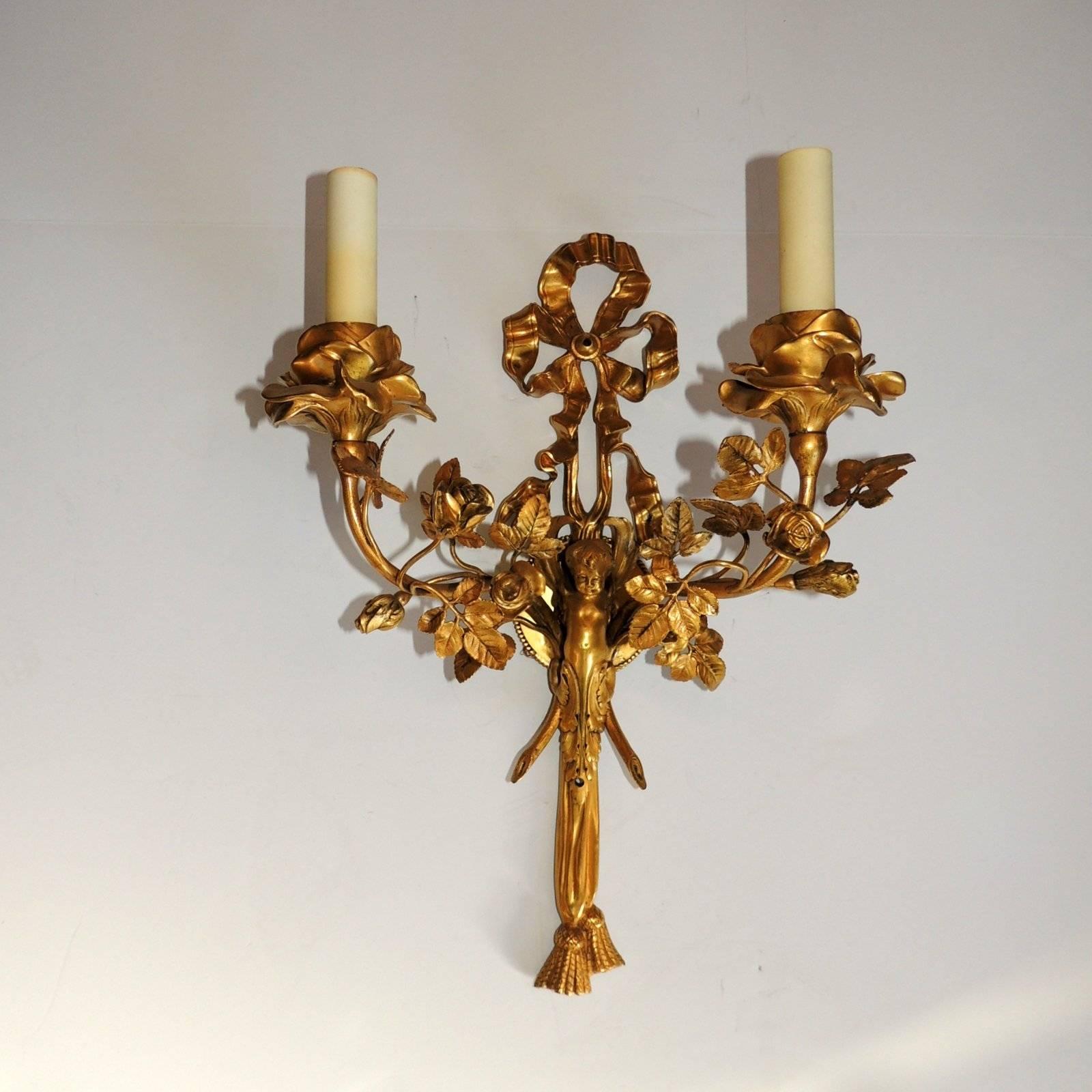 This elegant pair of signed Caldwell sconces are full of endearing details including the original doré Bronze finish. The top ribbon is a large bow over the putti centre with his charming face. Surrounding the two arms are beautiful roses including