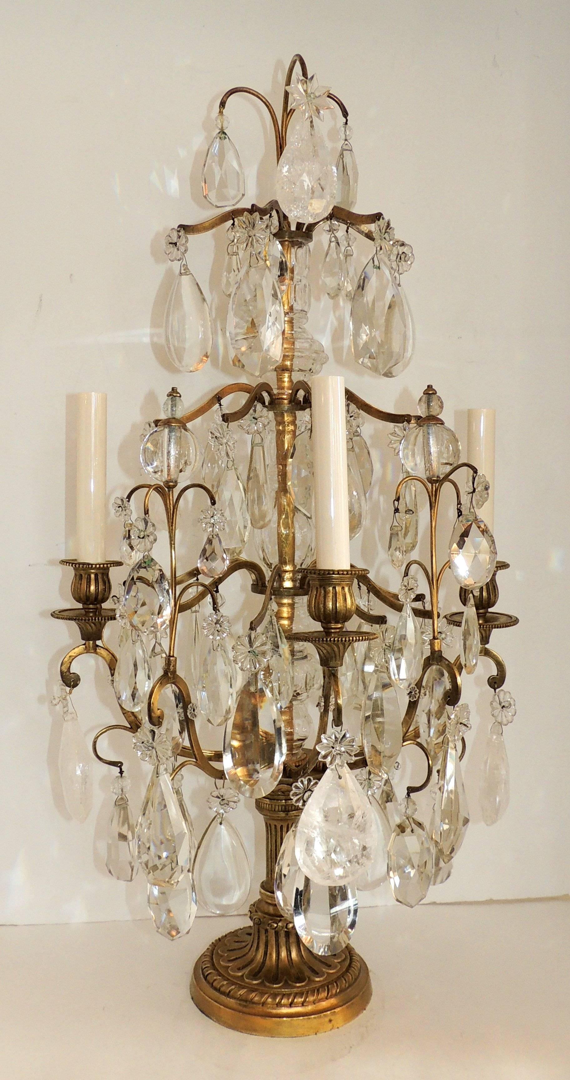 Pair of rock crystal and bronze three-light girandoles, candelabra. 
Beautiful rock crystals, stars and crystal prisms provide the charm of these wonderful girandoles with three lights and a flat back. The bronze center is encased in crystal and