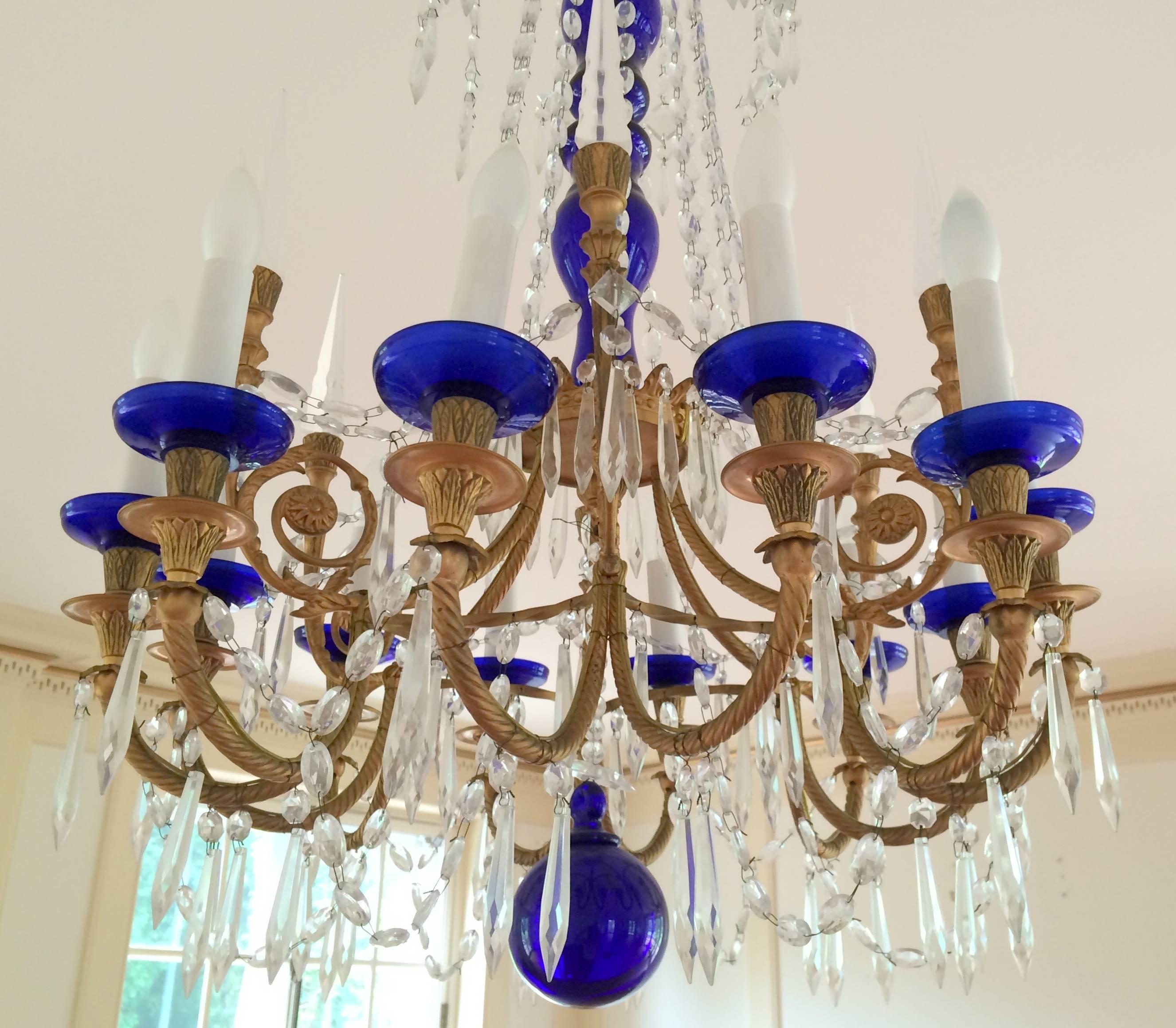 A wonderful pair of French doré bronze with cobalt blue center shaft, ball and accent cuos on each of the 12 lights, adorned with crystals to these Regency / neoclassical chandeliers.