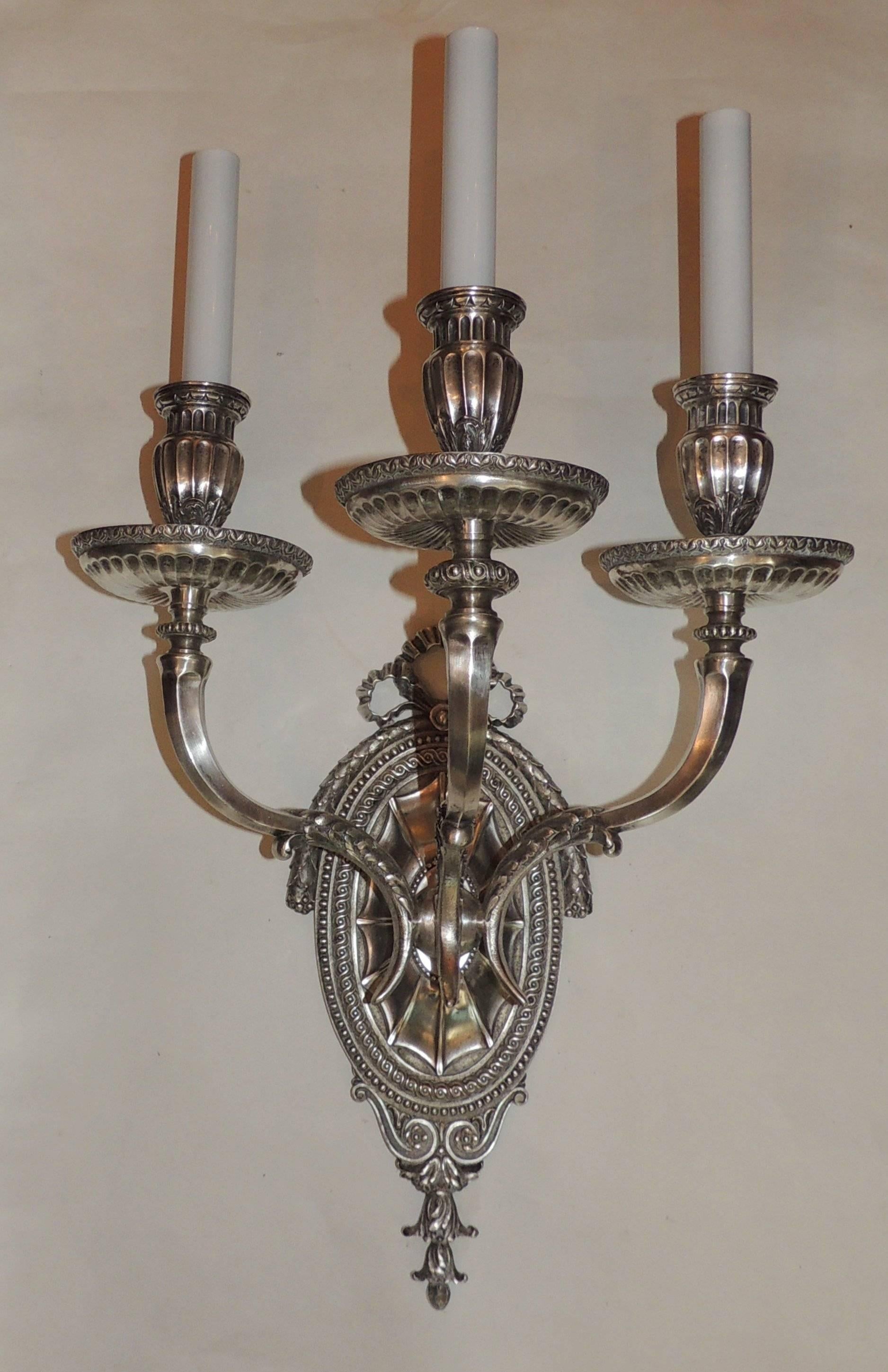 These wonderful silvered bronze three-arm sconces by Caldwell are beautifully detailed with a intricately detailed center medallion with draped filigree across the top and finished with a bow. The candle cups are finely fluted and decorated with