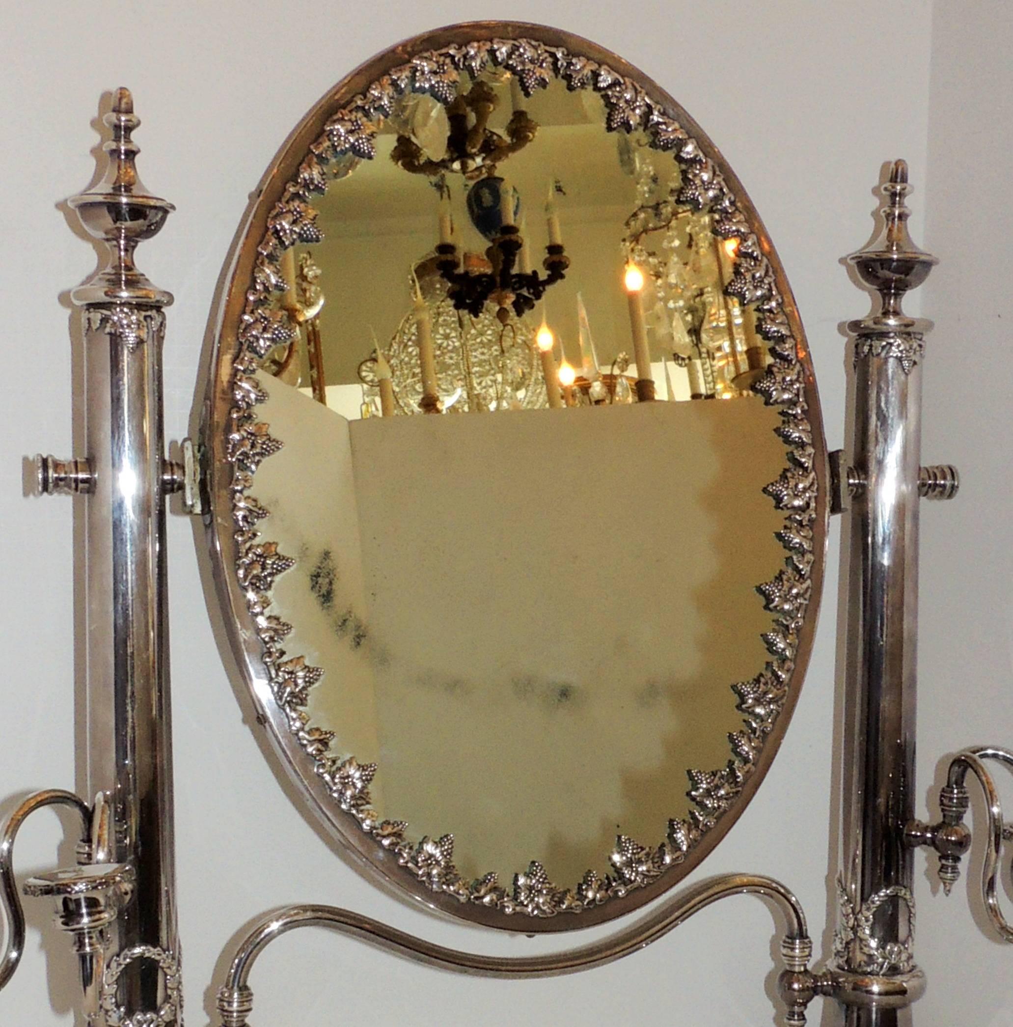 A wonderful English silver plated shaving or dressing mirror with a tiltable oval mirror framed by grapes on a vine, flanked by two- arm candelabra on either side, with a wreath detail.
The candelabra arms are adjustable and do move in and