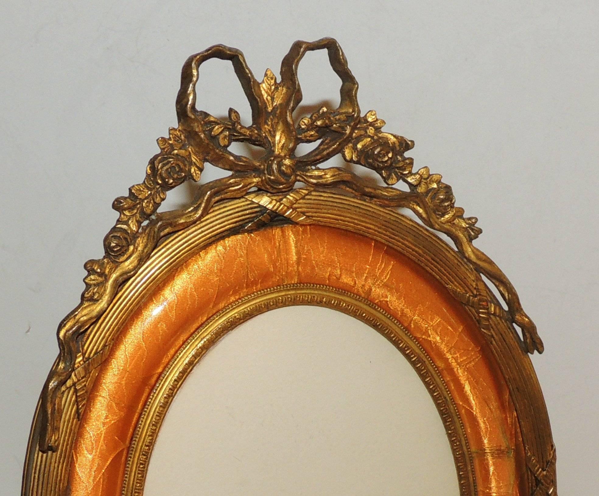 Vintage French bow top doré bronze oval picture frame with peach enamel frame with beautiful engravings and scroll details.
Original bronze stand.

Measures: 9.5