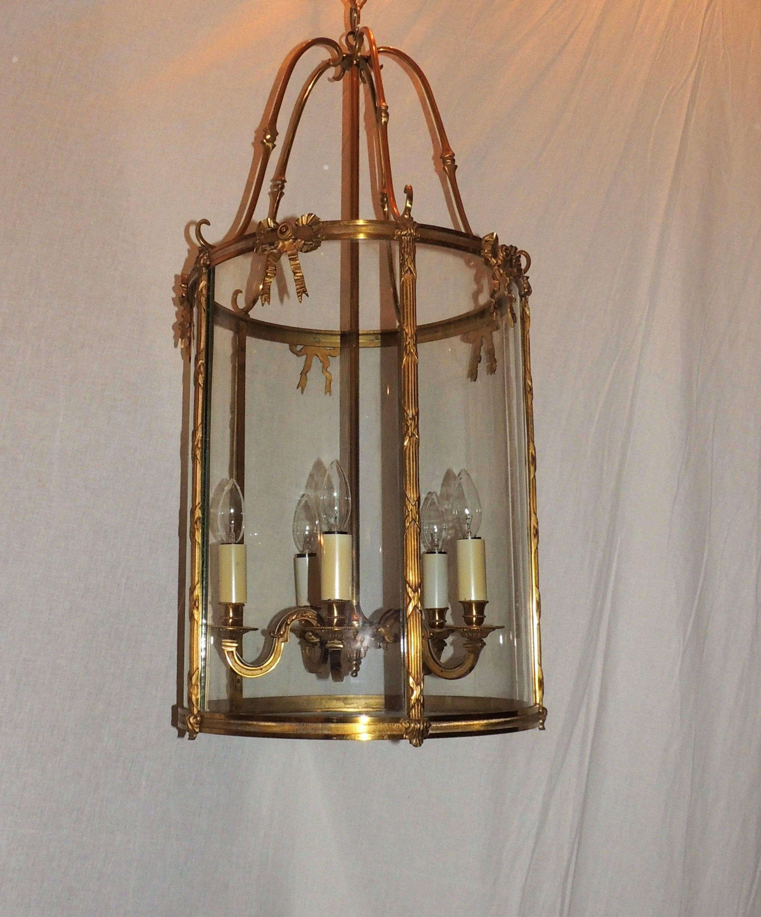 An elegant pair of doré bronze five-light lanterns with etched ribbed bronze trim on top and bottom of the lanterns are fluted reed trim with cross bows around a curved glass panel accented with bronze bows. Each of the fixtures have five arms with