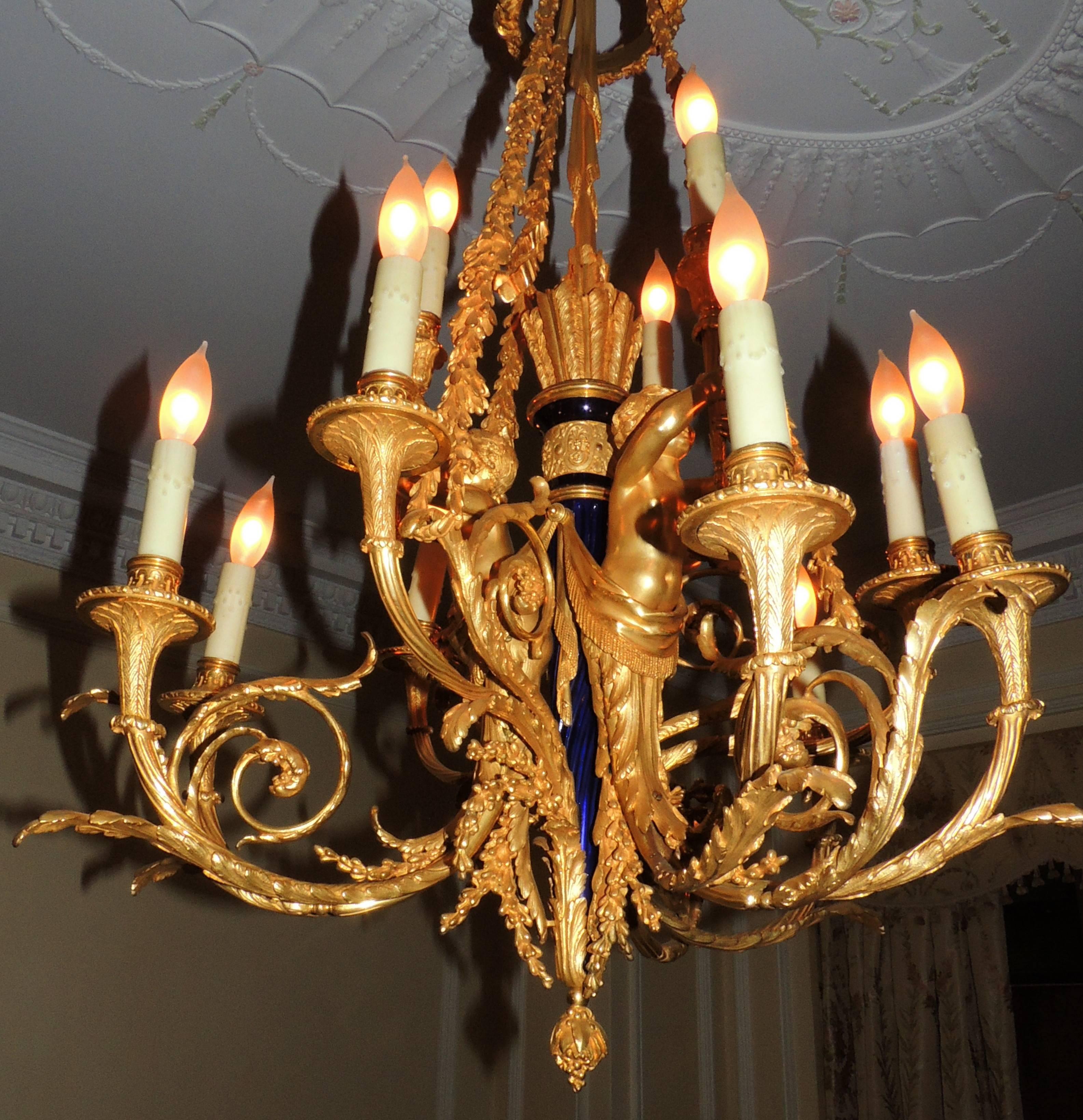 A very fine Louis XVI style gilt doré bronze cherub nine-light chandelier. The chandelier having elaborate acanthus scrolling arms issued from a classical torch stem with blue enamel, surmounted by four perching cherubs blowing trumpets.
This