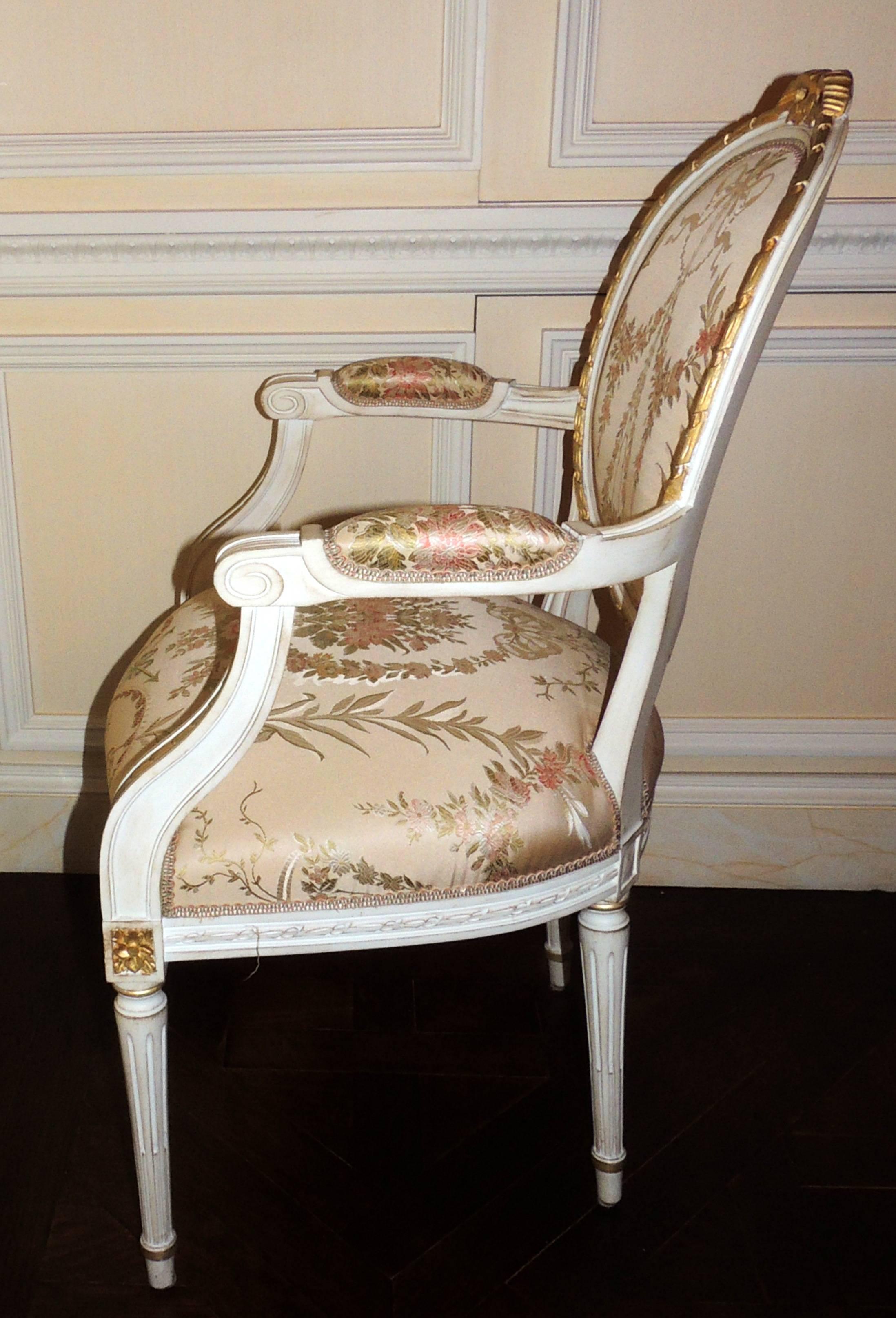 A wonderful set of Louis XVI French white and gold gilt oval back, fluted leg and bow top set of 14 chairs consisting of 12 sides and two arms with beautiful Scalamandre fabric.