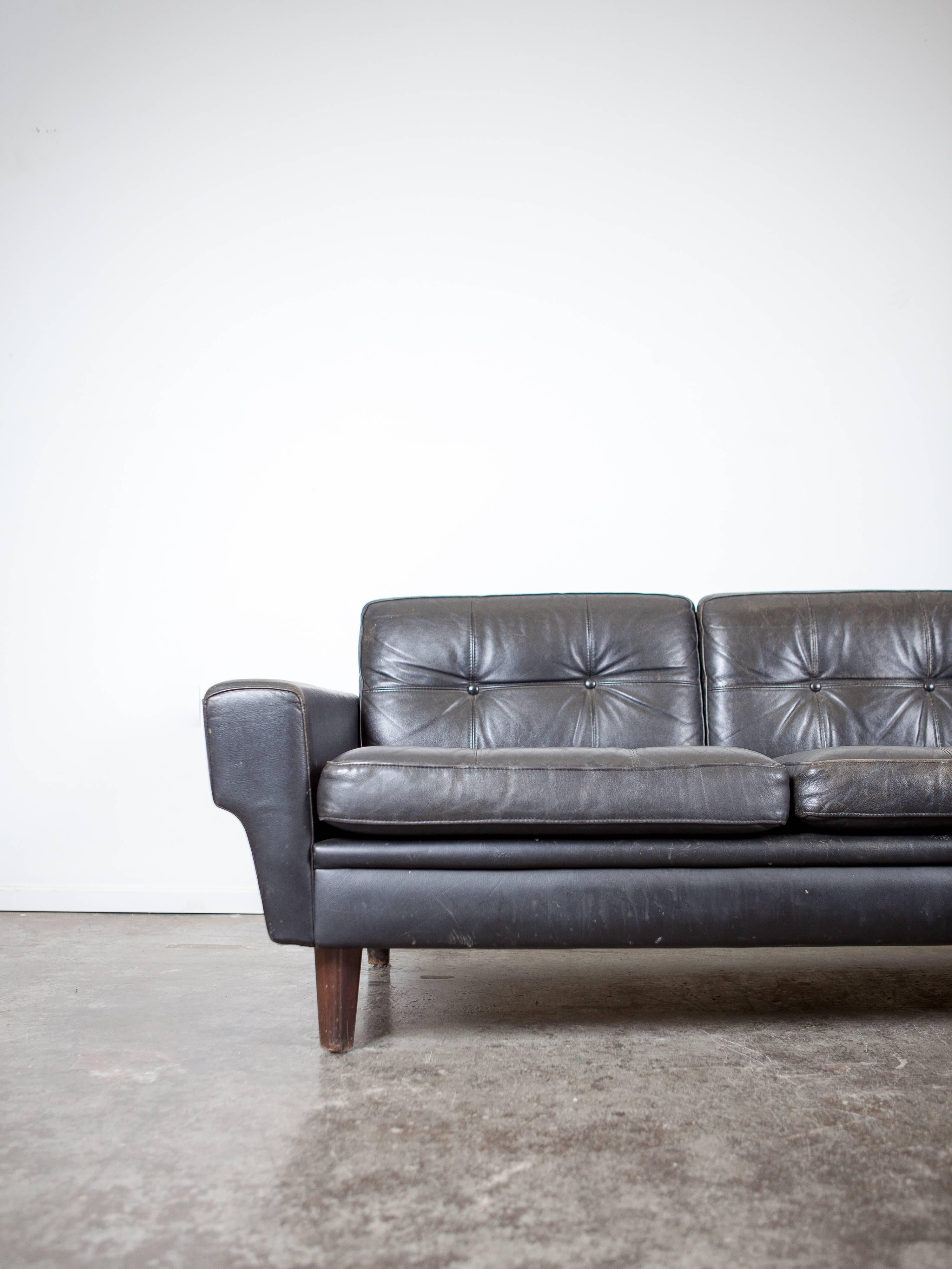 Classic Mid-Century Modern black leather sofa with button tufted cushions.