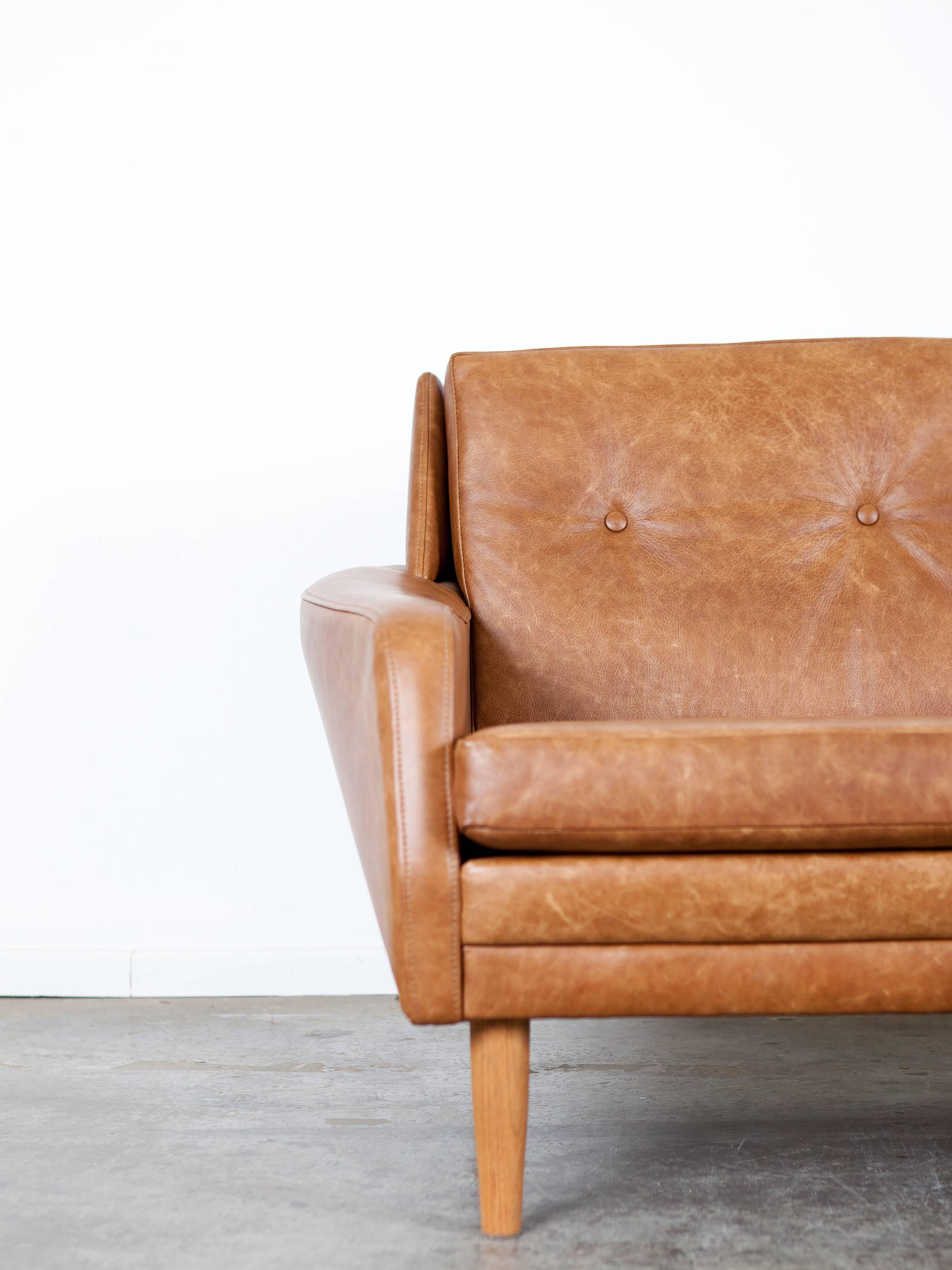 Classic button tufted cognac leather loveseat with Mid-Century Modern lines.