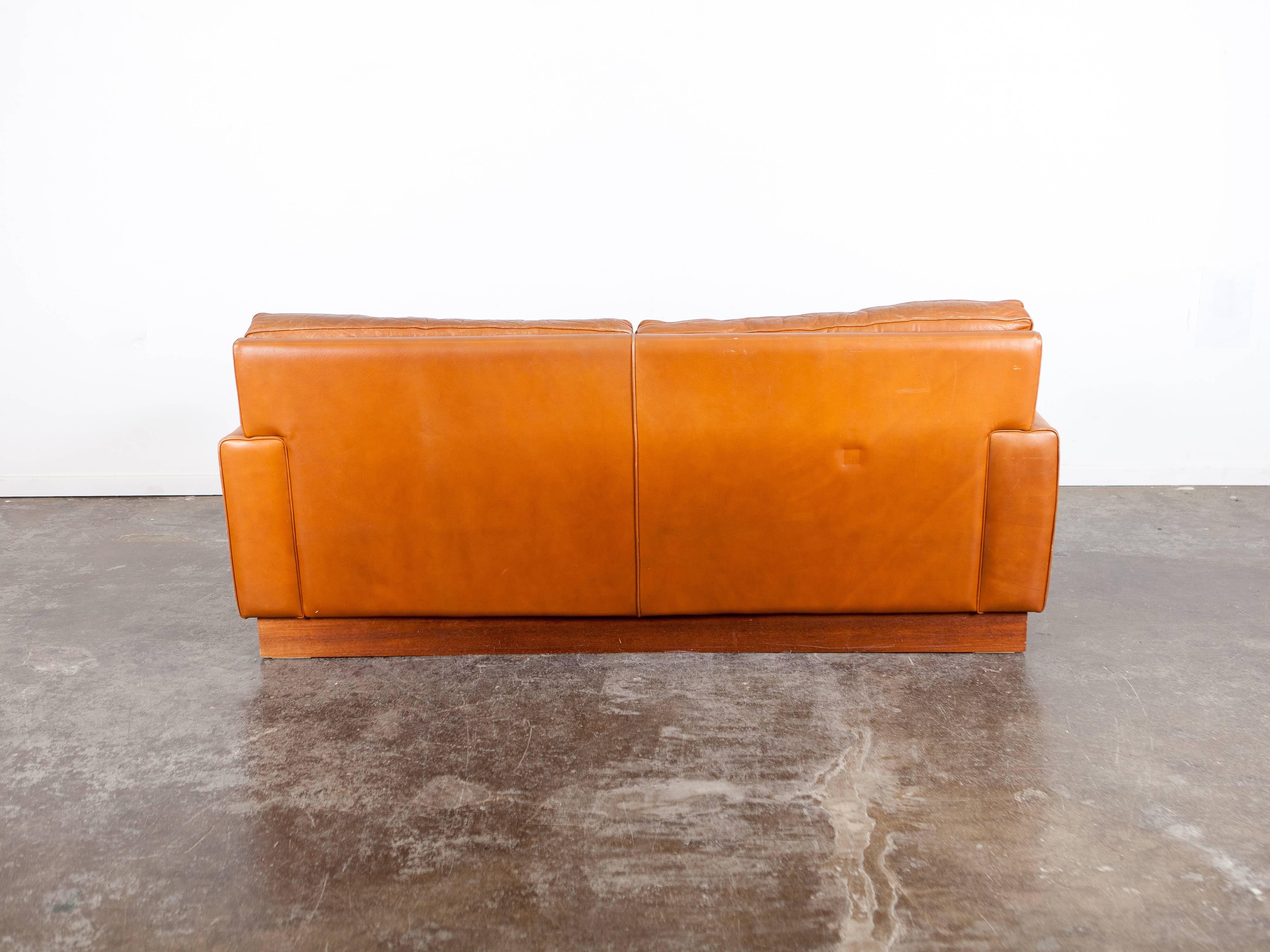 Two-seat tufted brown leather sofa on a plinth base by Arne Norell, produced in Sweden by Norell AB.
