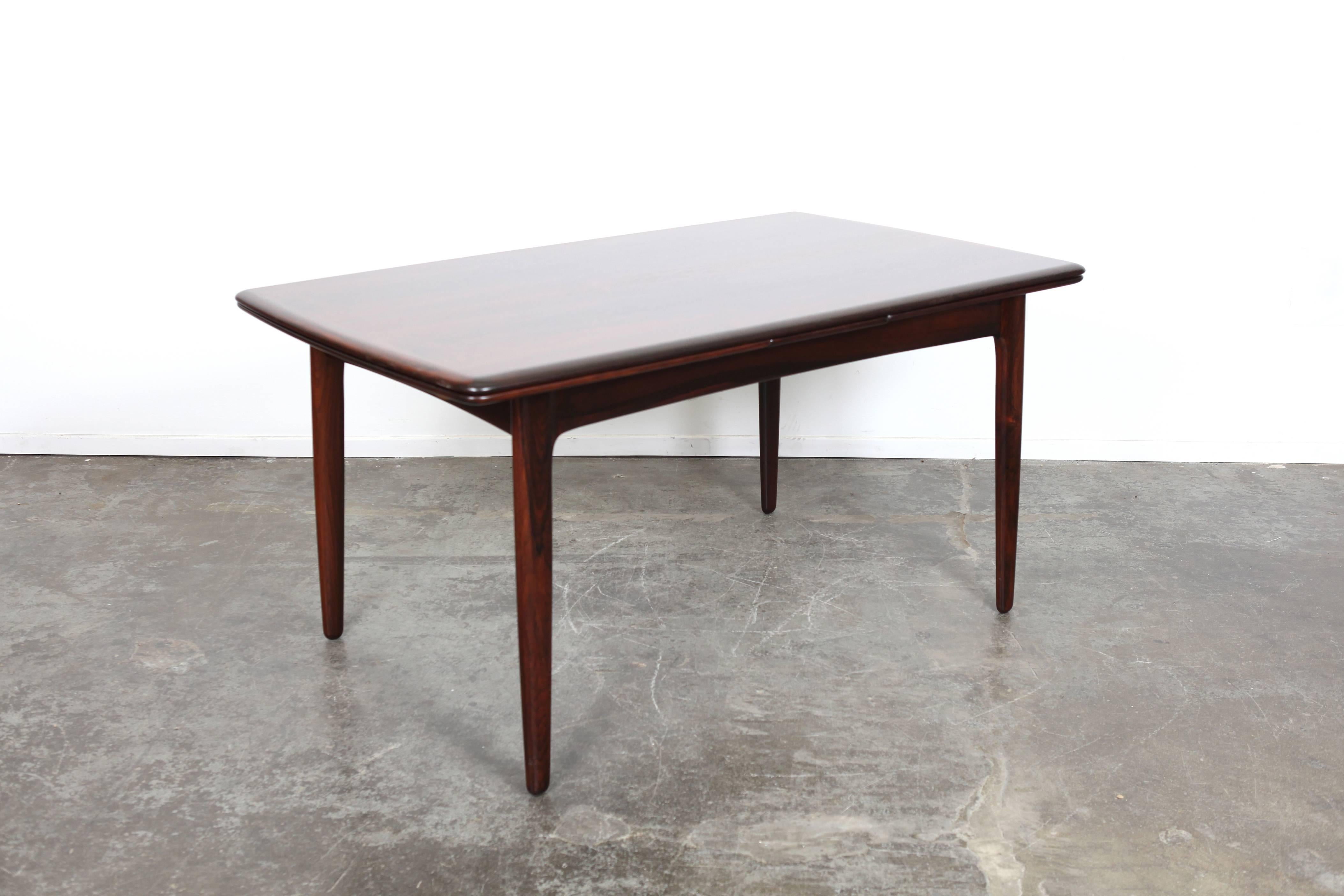 An elegant rosewood extendable dining table by Svend Åge Madsen for K. Knudsen. Featuring a beautiful grain pattern, solid rosewood legs and banding along with curved edge detailing giving it an overall organic aesthetic. The extended width is 101
