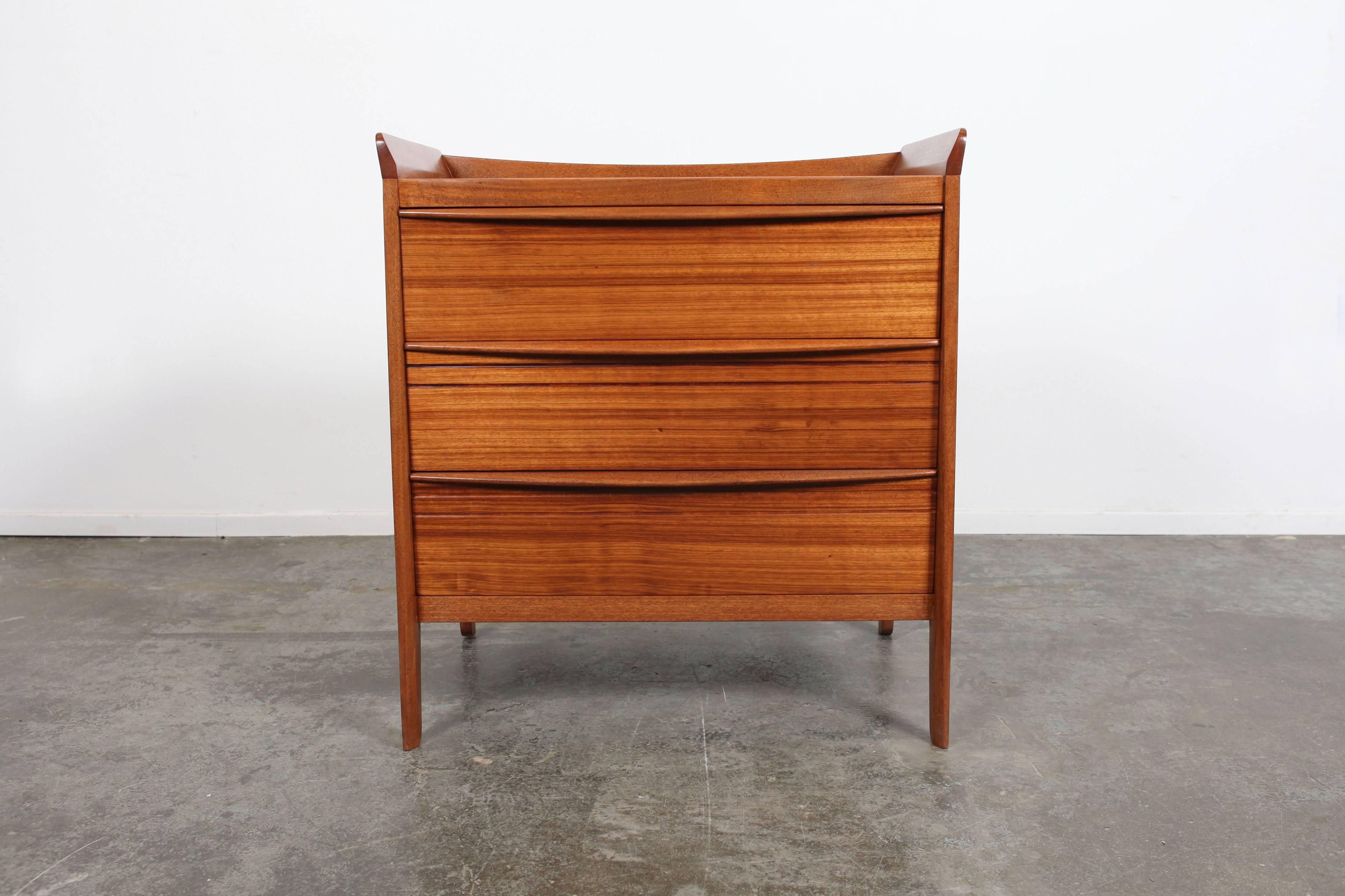 Mid-Century Modern dresser from England with silken mahogany veneer. This piece features a flared, raised border and contrasting side-paneling.