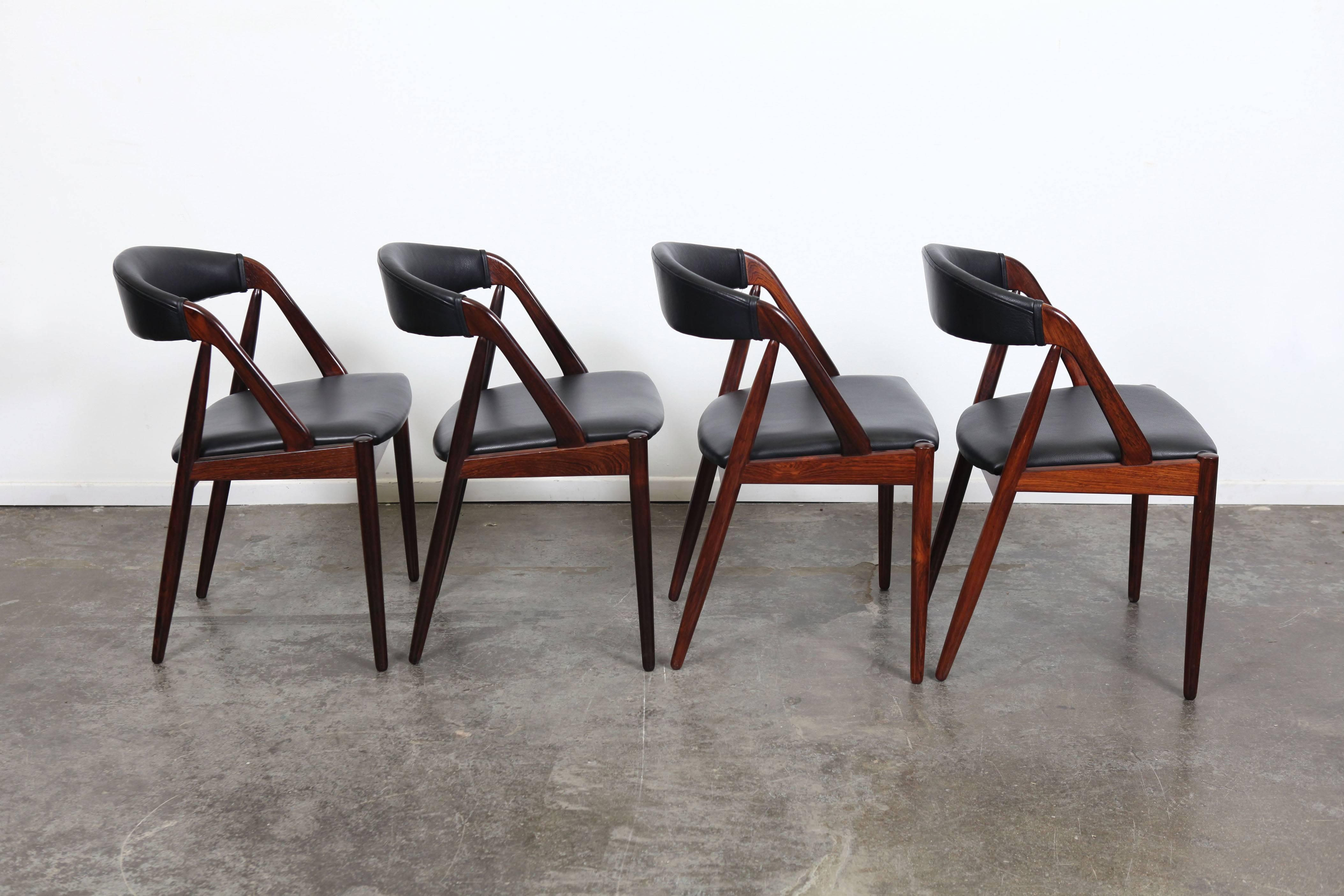 Set of four Danish Rosewood Kai Kristiansen Mid-Century dining chairs newly refinished in lacquer and newly upholstered in black leather.   These chairs feature vibrant wood grain and a softened angular design.