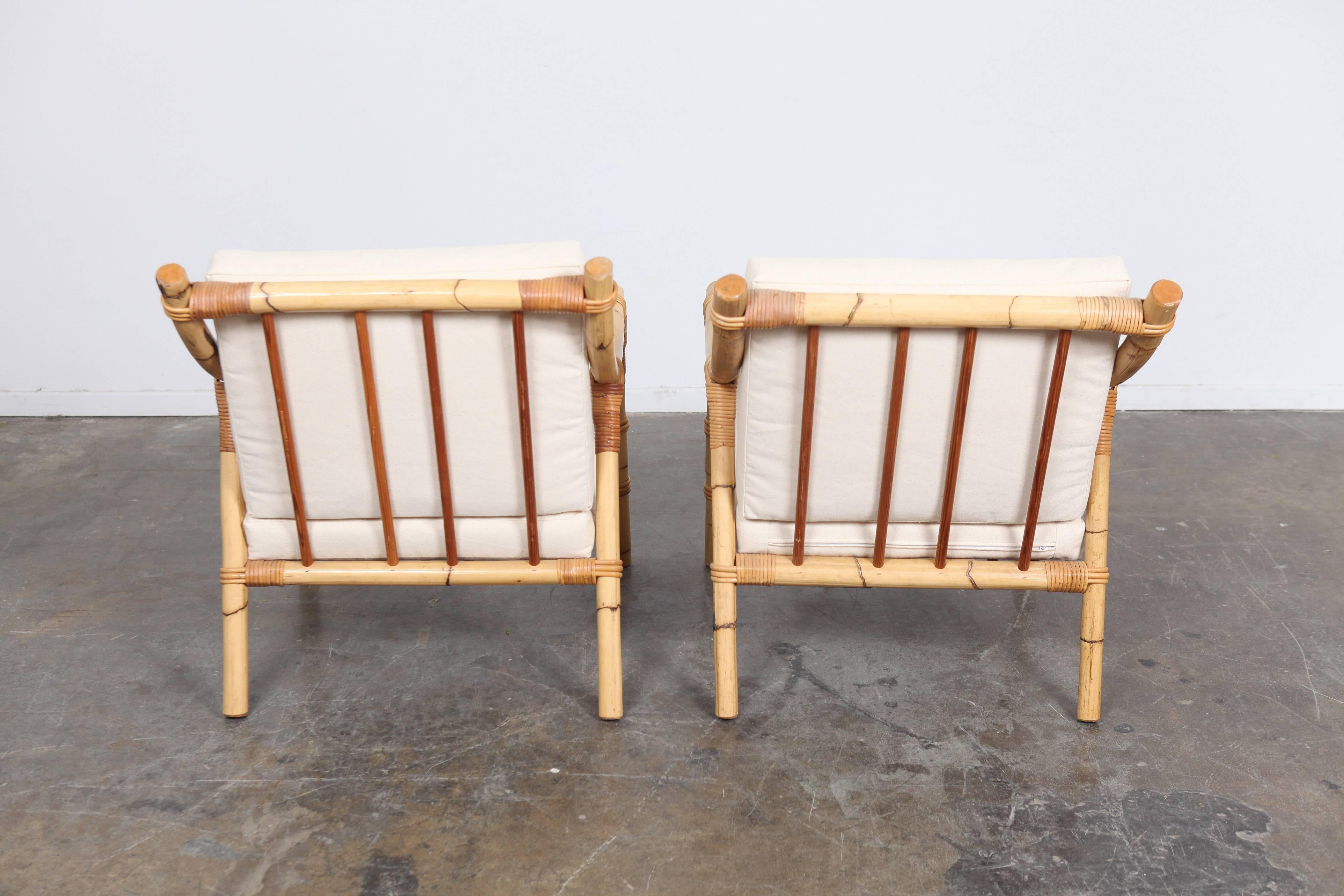 Set of two unique Mid Century rattan or bamboo lounge chairs with new cream upholstery and loose cushions.