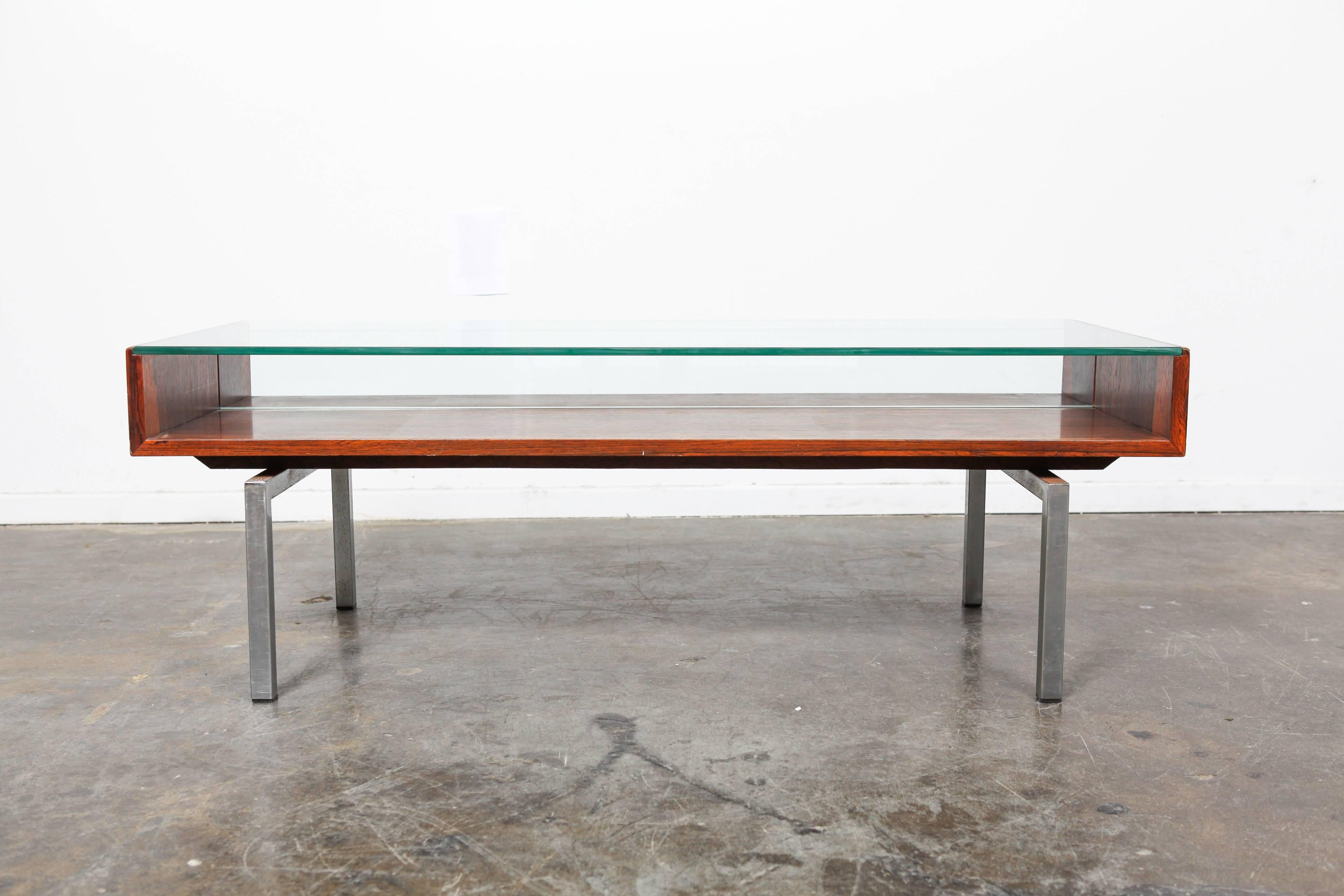 1960s Danish Mid-Century Modern rosewood coffee table with a raised glass featuring display storage underneath. This piece stands on angular bar chrome legs.