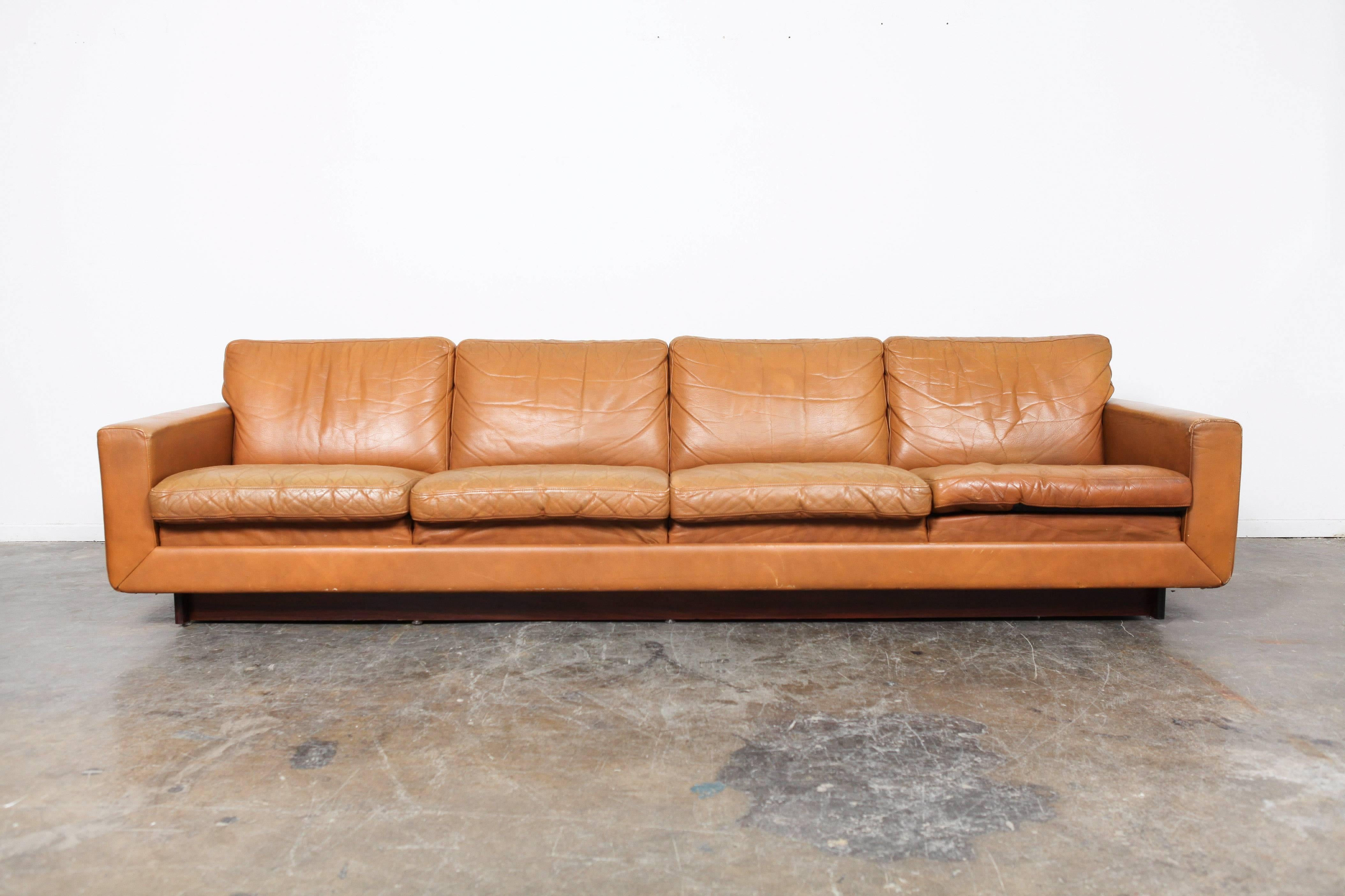 Classic Danish Mid-Century Modern sofa in camel colored leather with loose back and seat cushions. This piece rests on a wooden plinth base and has excellent patina throughout.