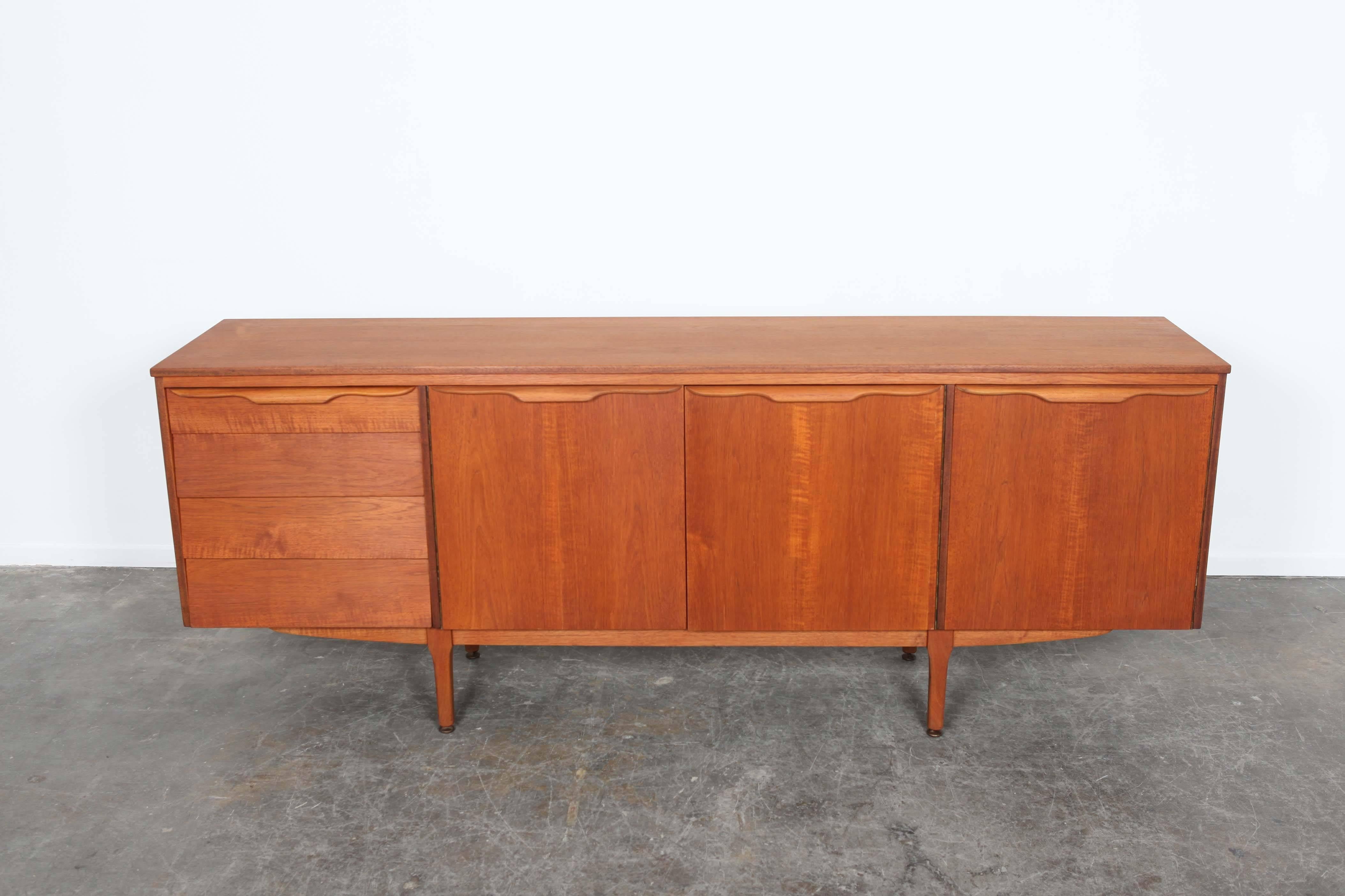 Teak four-drawer sideboard from England. One large center compartment and one smaller compartment with shelf. Front of drawers are angled. Newly refinished.