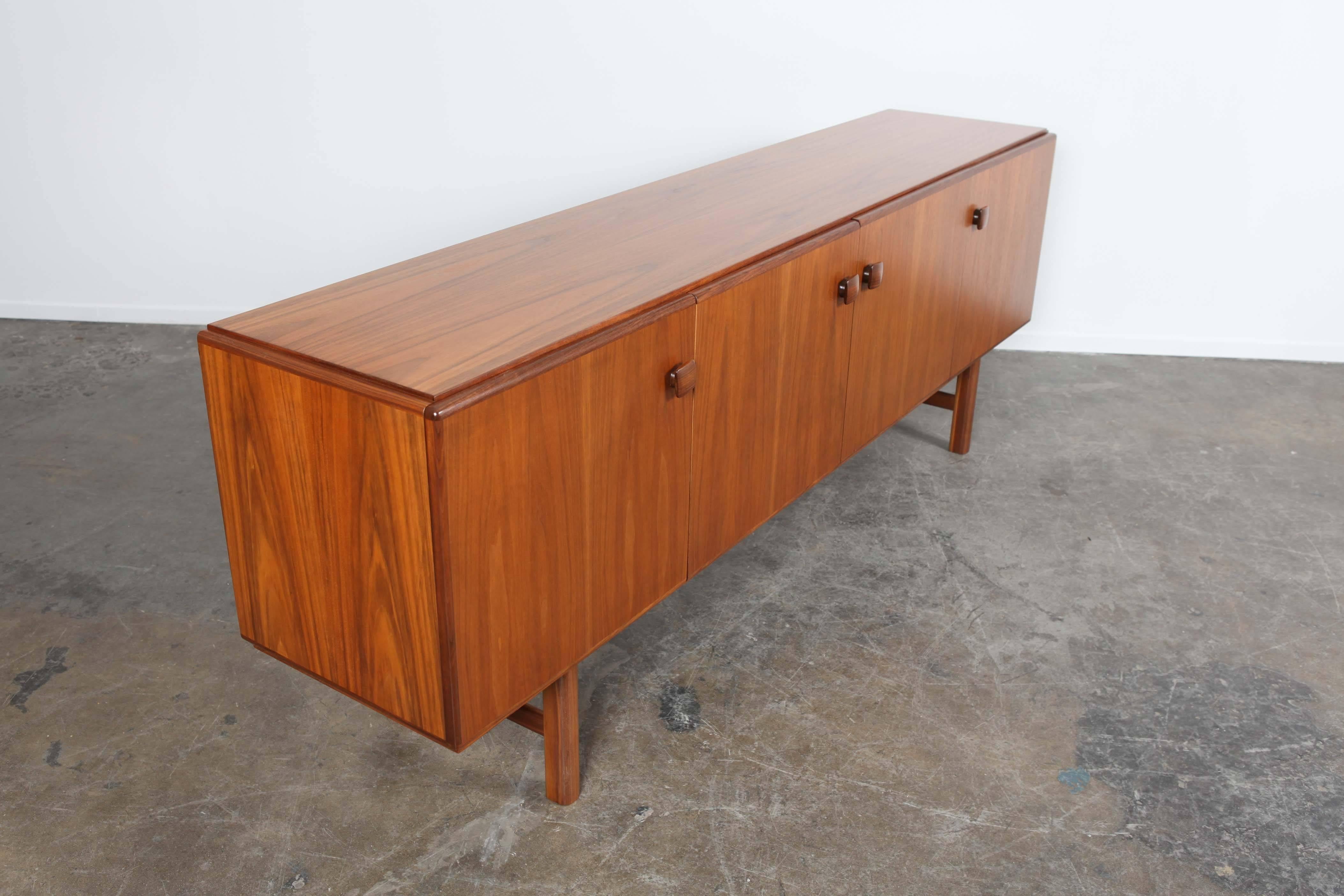Swedish Mid-Century Modern low, walnut sideboard with four cabinet style doors that have twisting handles which lock each door. All 4 sections have shelving storage in them and one has an additional two upper interior drawers. Model "Number