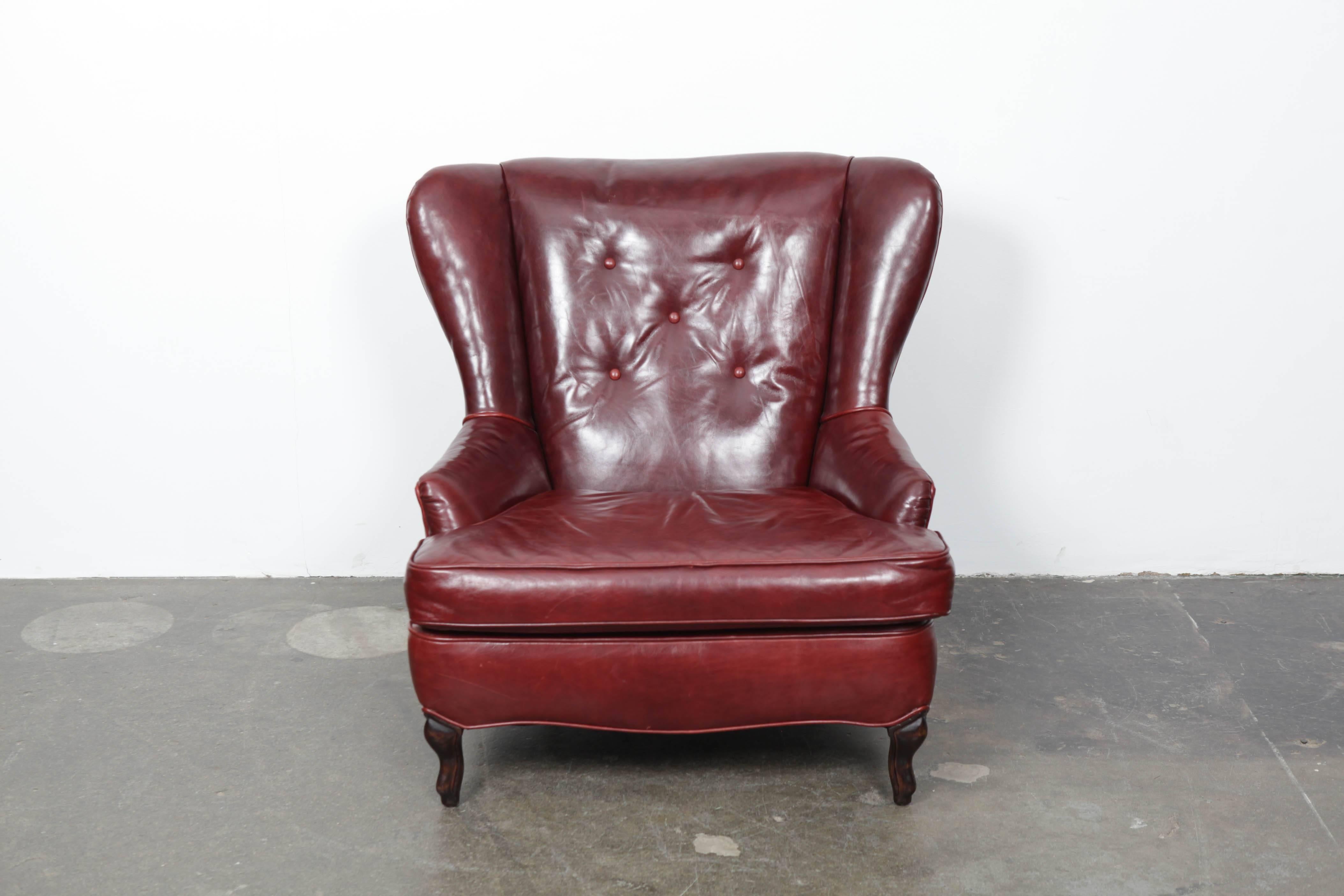 American made oxblood leather wing back chair with excellent patina and wear, walnut legs (cabriole legs in front and curved back legs) and a button tufted back cushion.  Sizeable chair. 