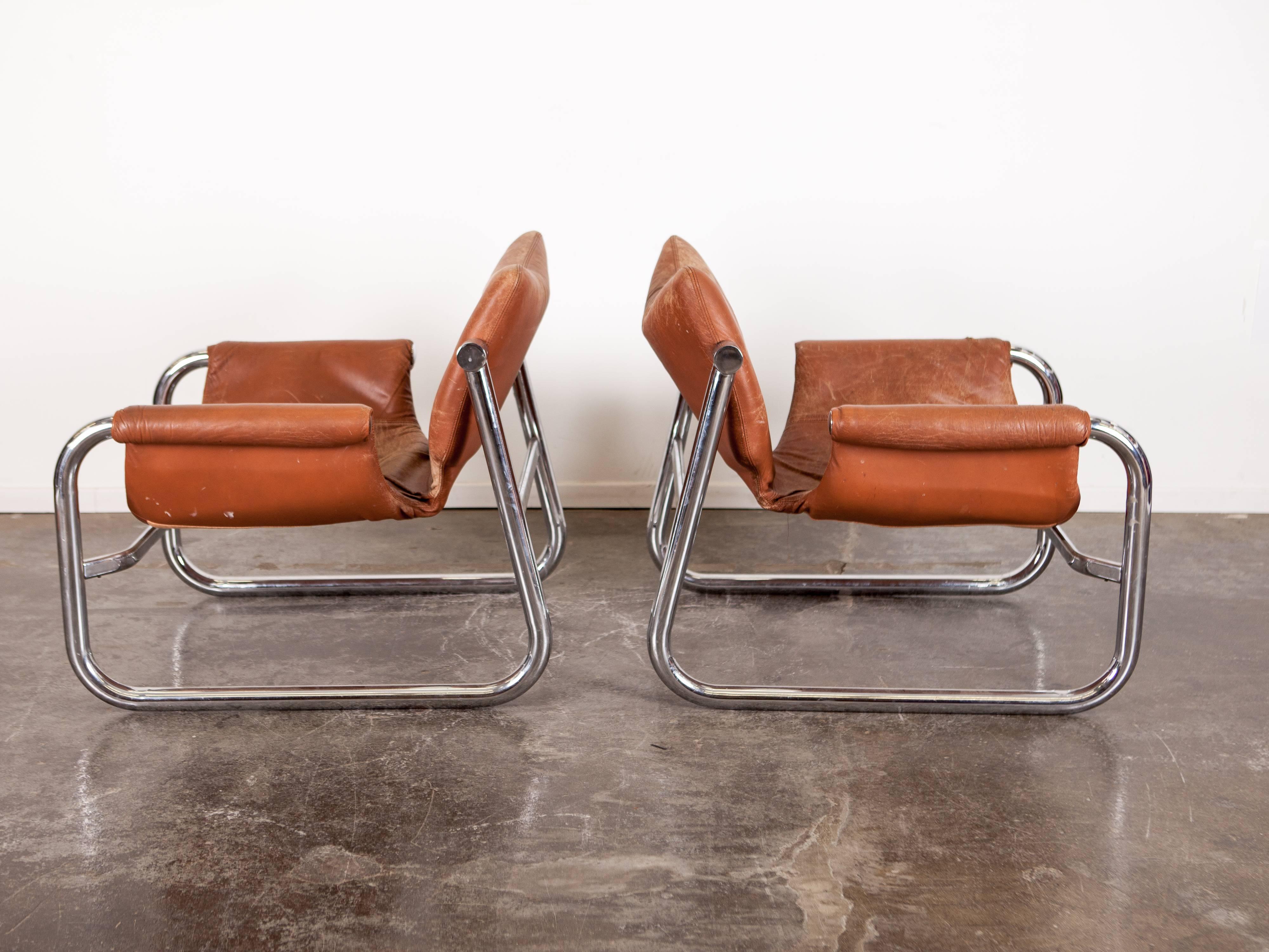 Pair of chrome and brown leather chairs with a sling seat with a pivoting back, designed by Maurice Burke, called the 'Alpha Chair'. Very nice patina on the leather, they were manufactured by Pozza Brazil.