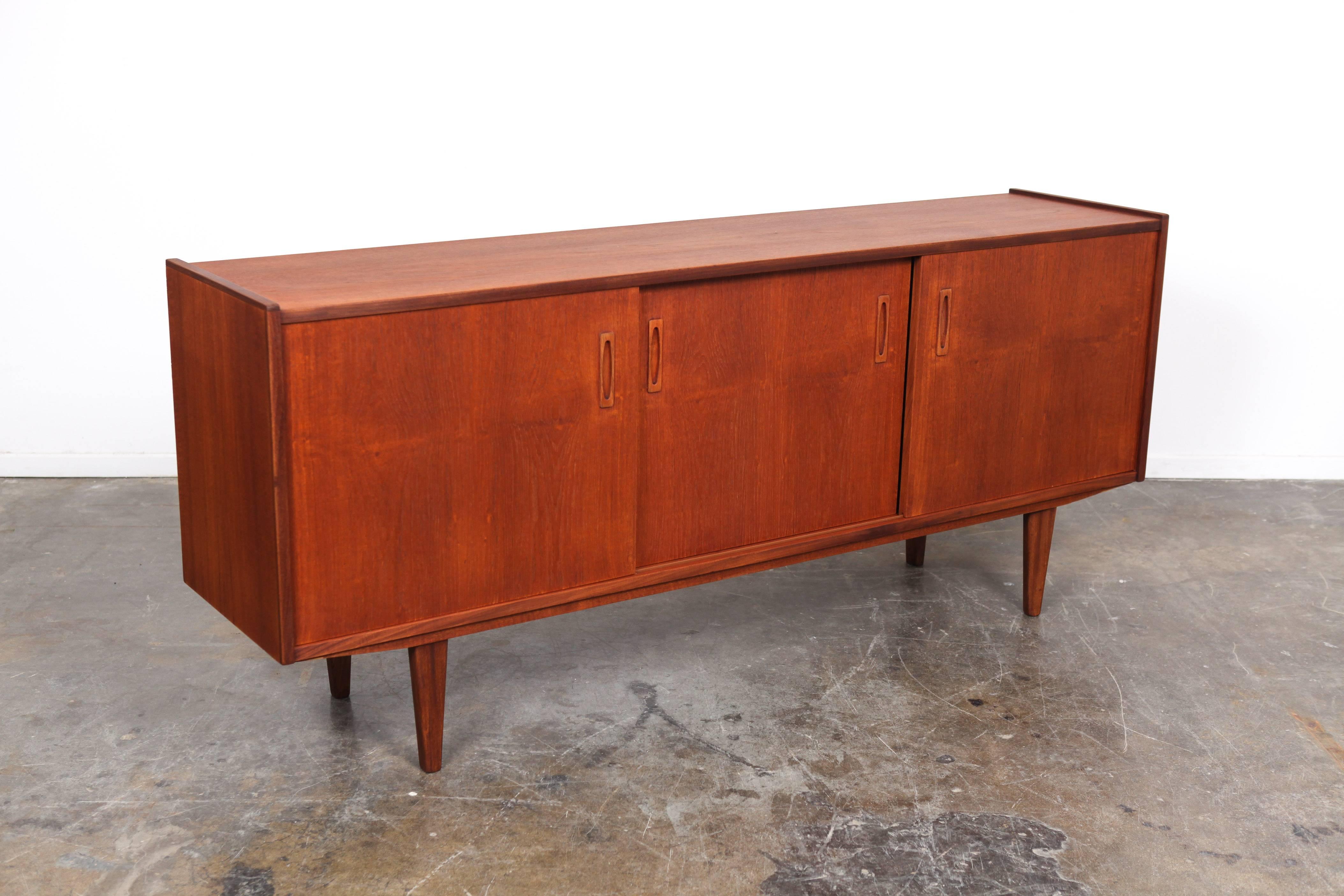 Danish teak three door (sliding) sideboard with Classic Mid-Century pulls, 1960s. This piece features a felt lined cutlery drawer and is supported by tapered teak legs.
 