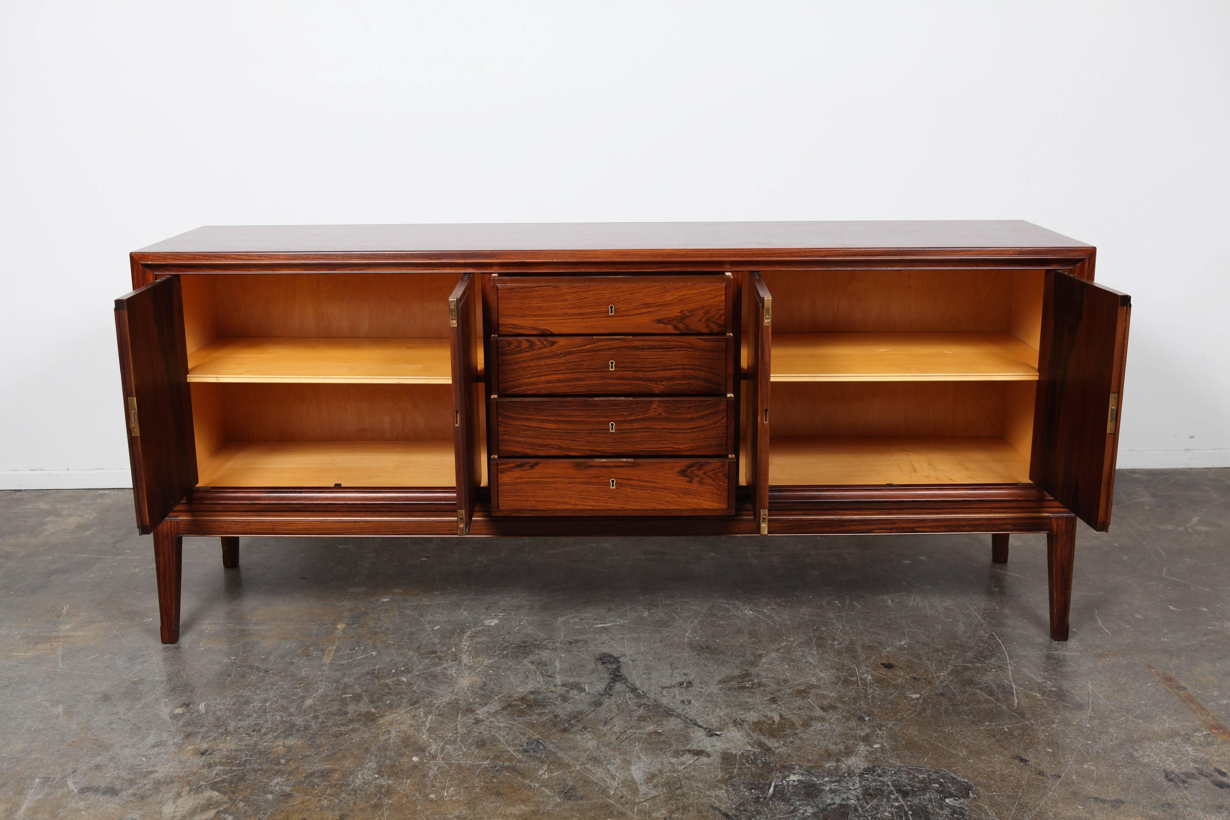Mid-Century Danish Modern rosewood sideboard with clean lines and bookmatched wood grain. This piece has four locking drawers and two side cabinets with a single interior shelf.
