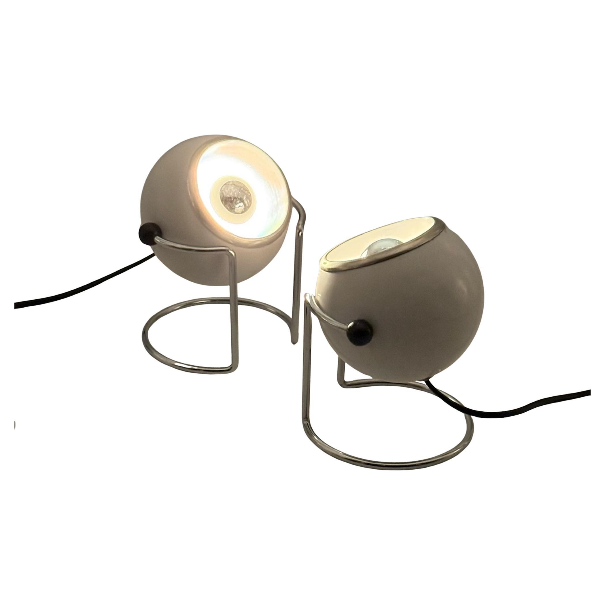 Este par de lámparas Targetti con forma de globo ocular de los años 70 ejemplifica la estética atrevida y funcional de la iluminación italiana de la Era Espacial. Cada lámpara está diseñada con un cabezal esférico lacado en blanco, pomos laterales