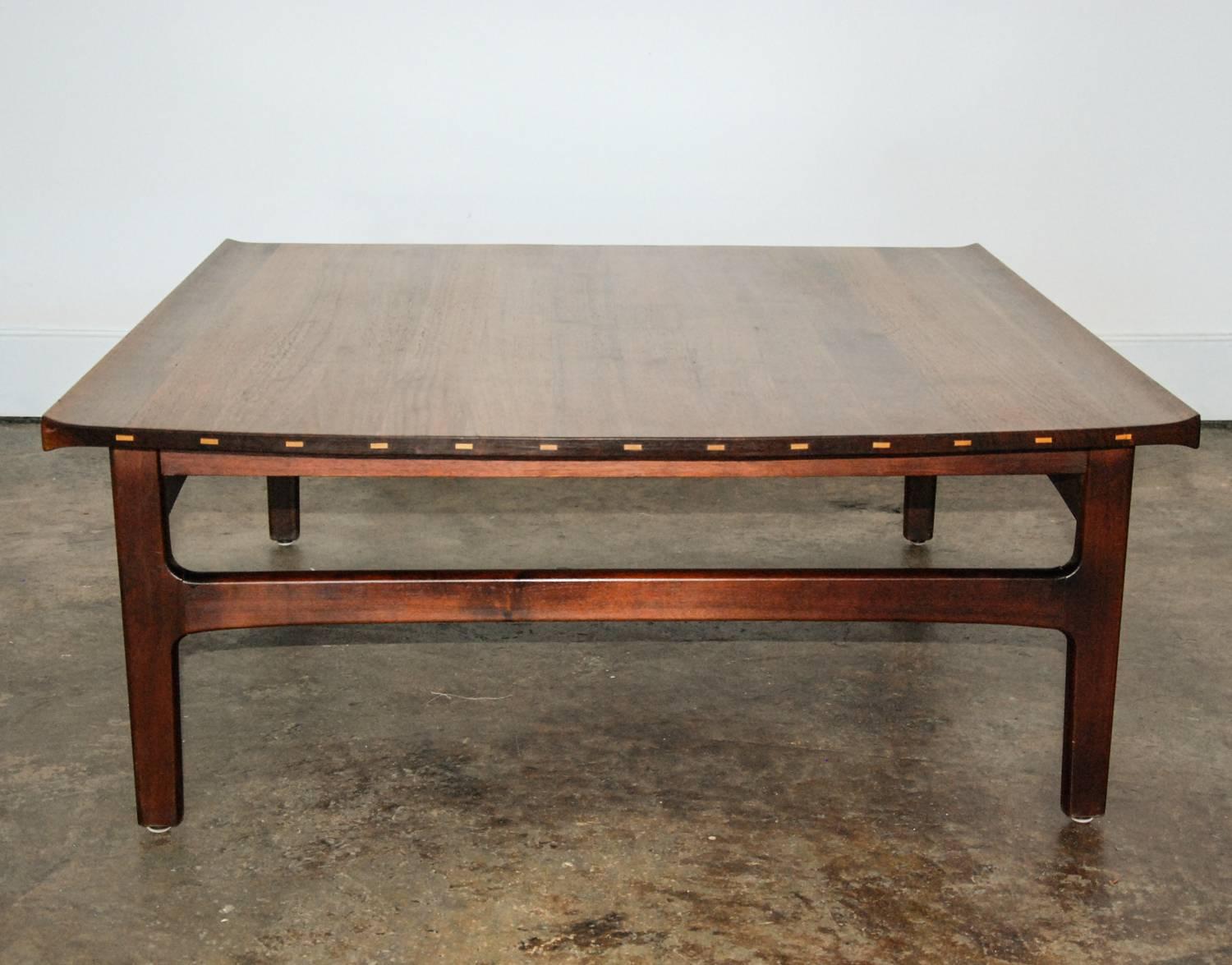 A fine Dux of Sweden richly grained teak coffee table of mortise and tenon construction with incised sycamore detailing on the top edge.  The upturned top and inset legs hint towards an Asian aesthetic.  The underside of the table top has the
