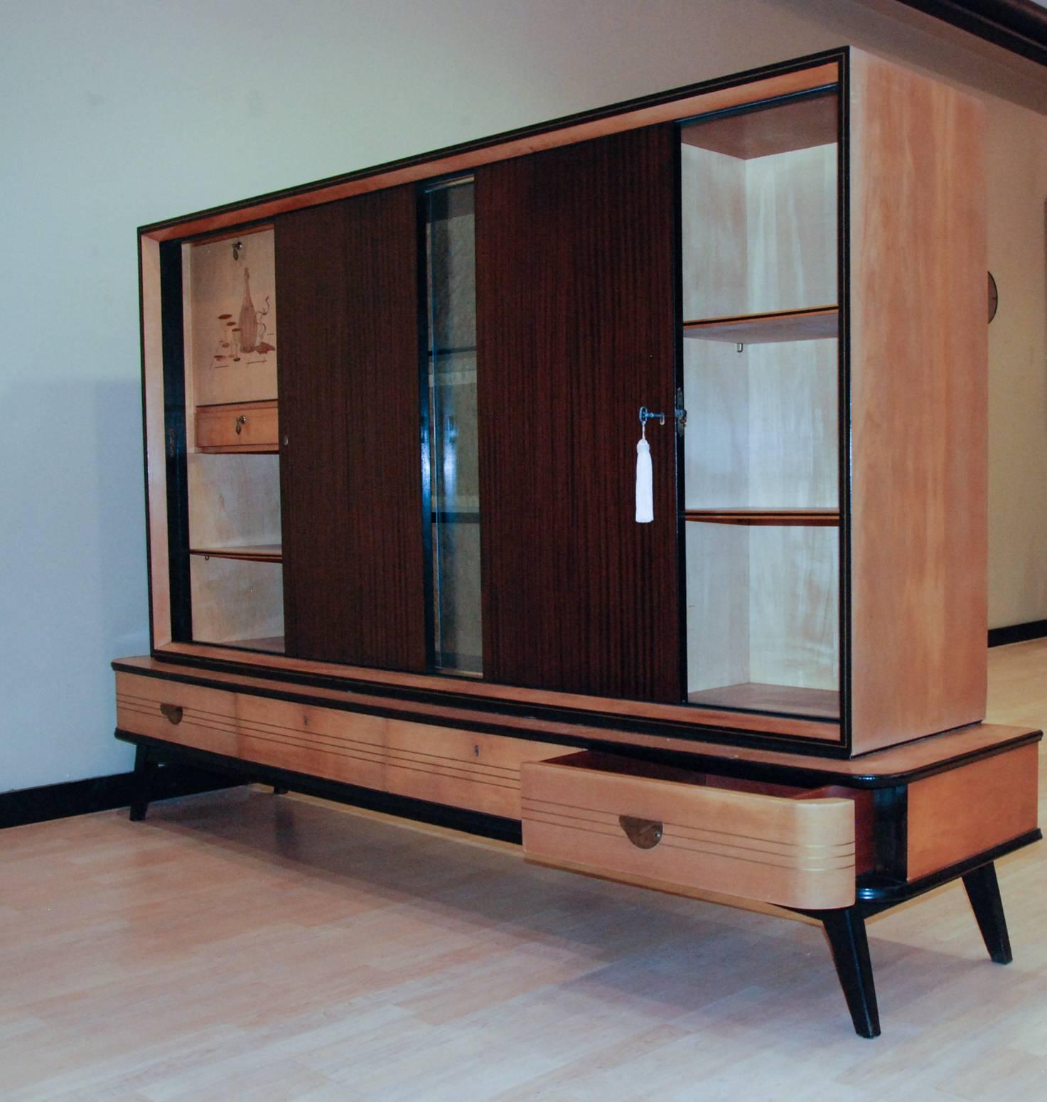 A fine German bar and display cabinet in various exotic woods with a marquetry still life design on the pull-down bar door. The interior is mirrored with a glass shelf and interior light. The unit separates into two sections for easier transport