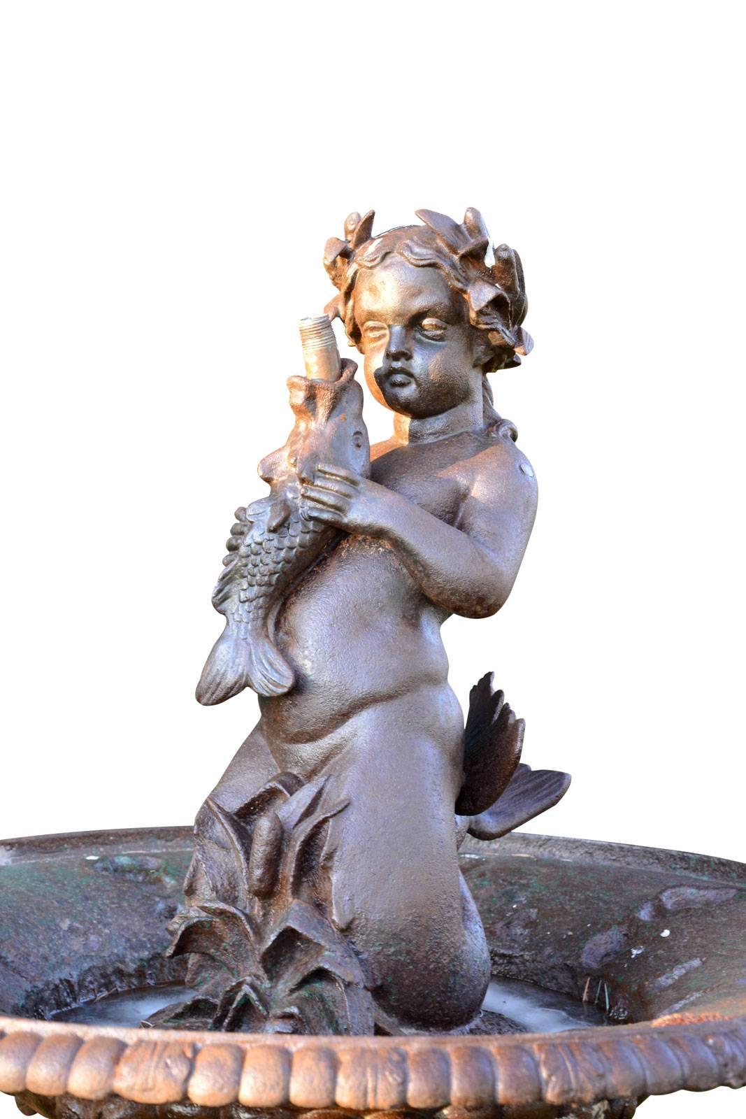 Dating from the late 19th century, cast iron fountain centerpiece decorated with triton crowned laurel holding a fish in his hands. The gadrooned basin is supported by a turned feet lavishly decorated with flowers, acanthus leaves ending with a