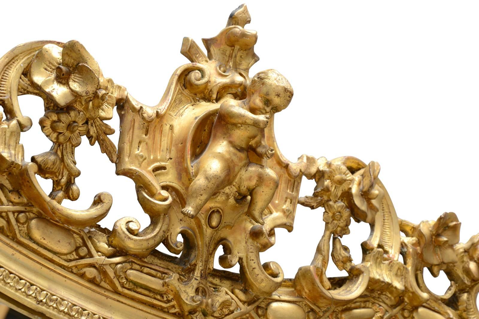 Dated from the 19th century, Napoleon III period gilded wood and stucco mirror. A double frieze of pearls and interlacing adorn the edge of the mirror. A putto at the center of a cartouche flanked by foliages, flowers and leather-cut elements