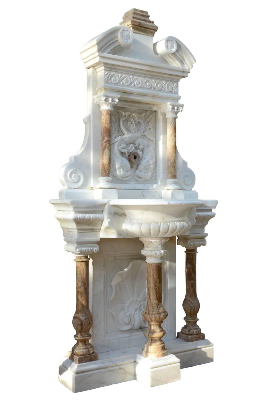 Dated from the 19th century, white Carrara marble and onyx wall fountain. The base, consisting of three onyx baluster columns and Ionic capital, rests on a molded base. The Carrara marble background of base, presents a carved shell decor. A