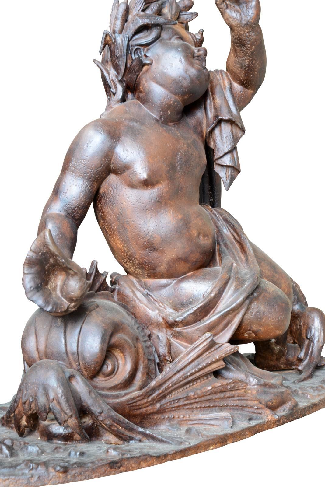 Dated from the 19th century, circa 1880, a cast iron aquatic group with a putto crowned with reeds and delicately dressed in a simple drape, riding a dolphin. He holds a shell in his right hand, while the left seems to move over his head.

The