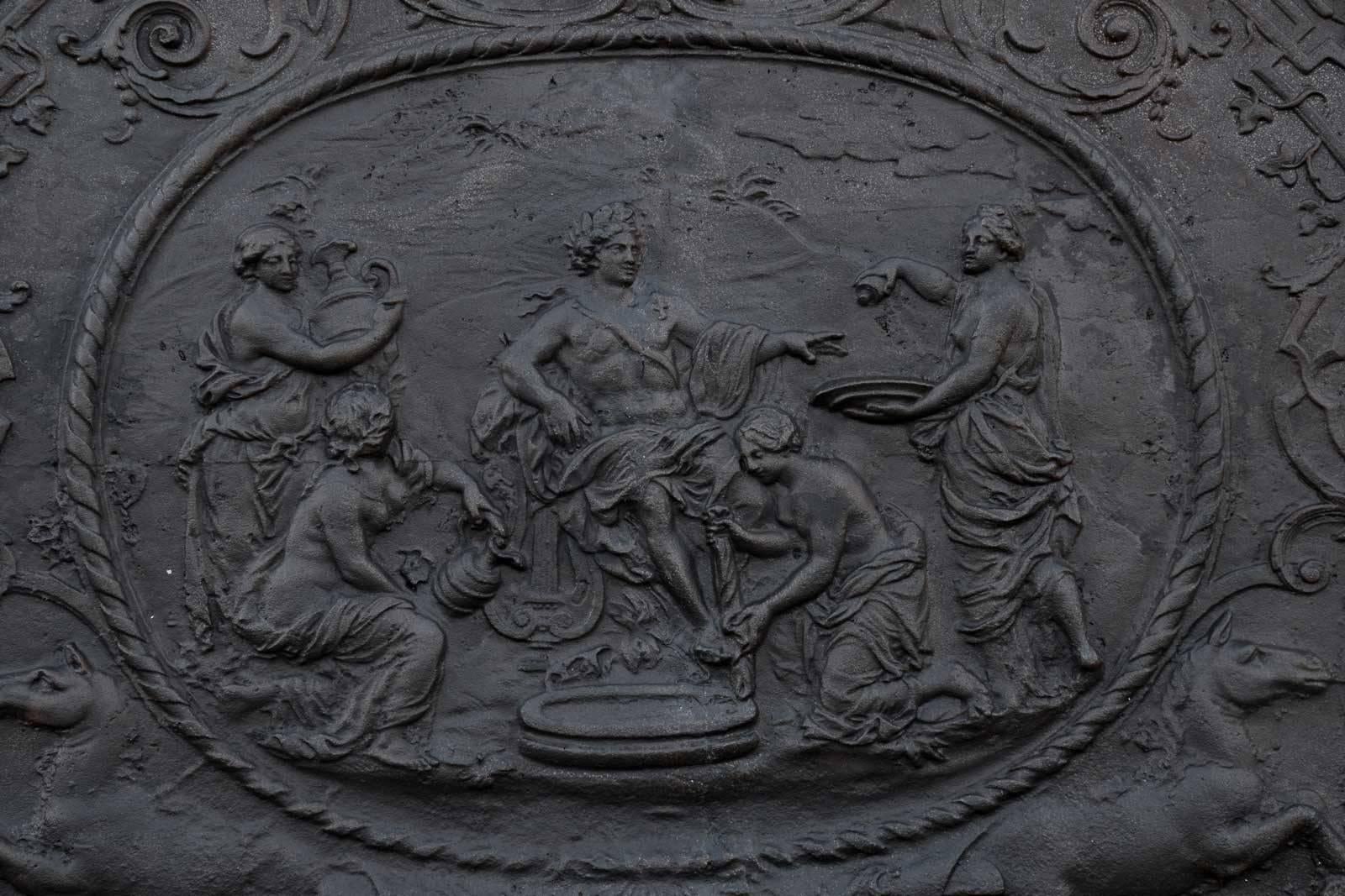 Cast iron fireback from the early 18th century and representing in a medallion Apollo served by the Nymphs. A decoration with foliage and arabesques decorate the rest of the fireback which are also present, supporting the medallion, two horses. This