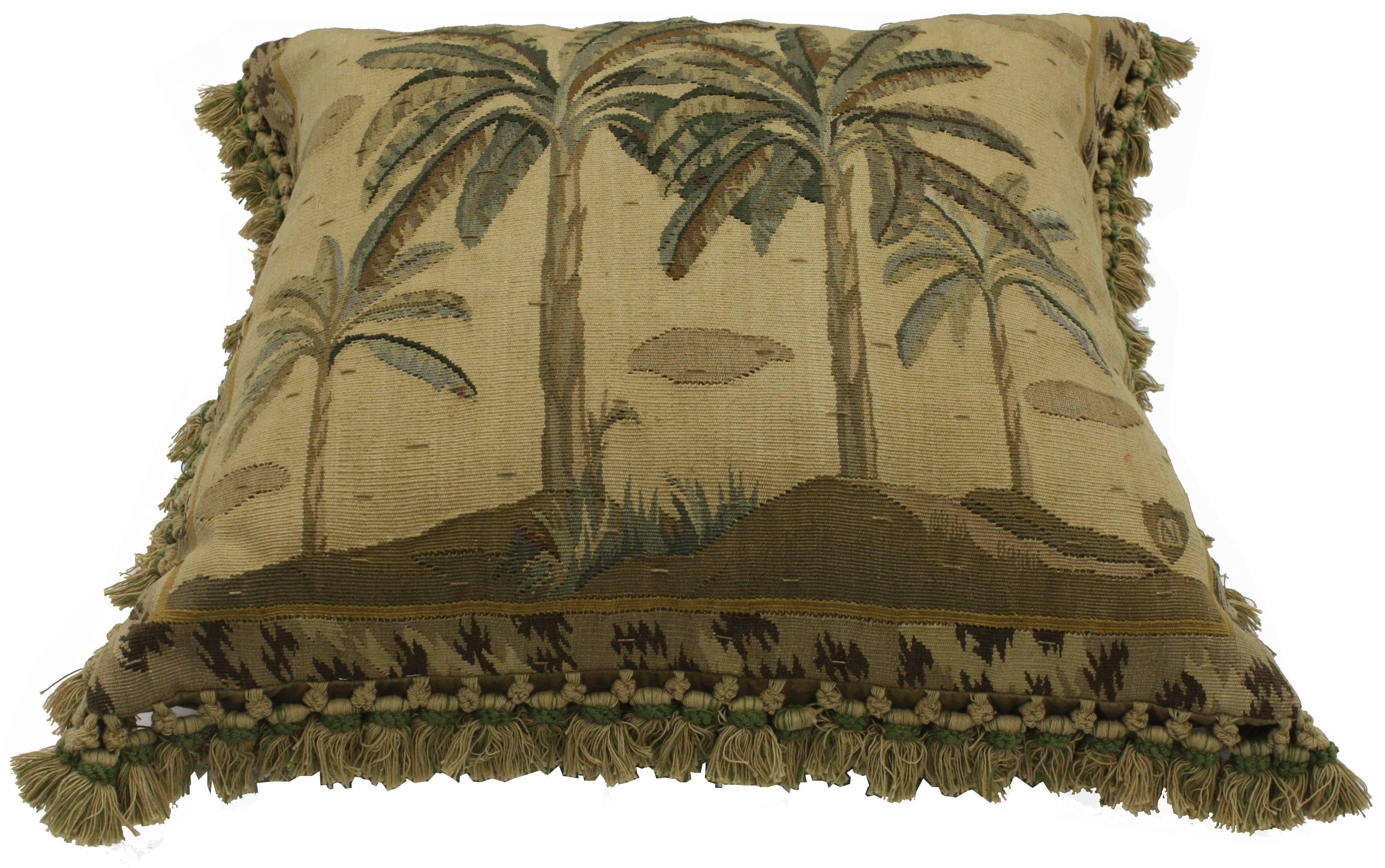 Add a tropical and exotic aesthetic to your space with this late 19th century antique European tapestry pillow with French Passementerie fringe. A decorative landscape scene of palm trees rendered in rich and refined colors ranging variegated shades