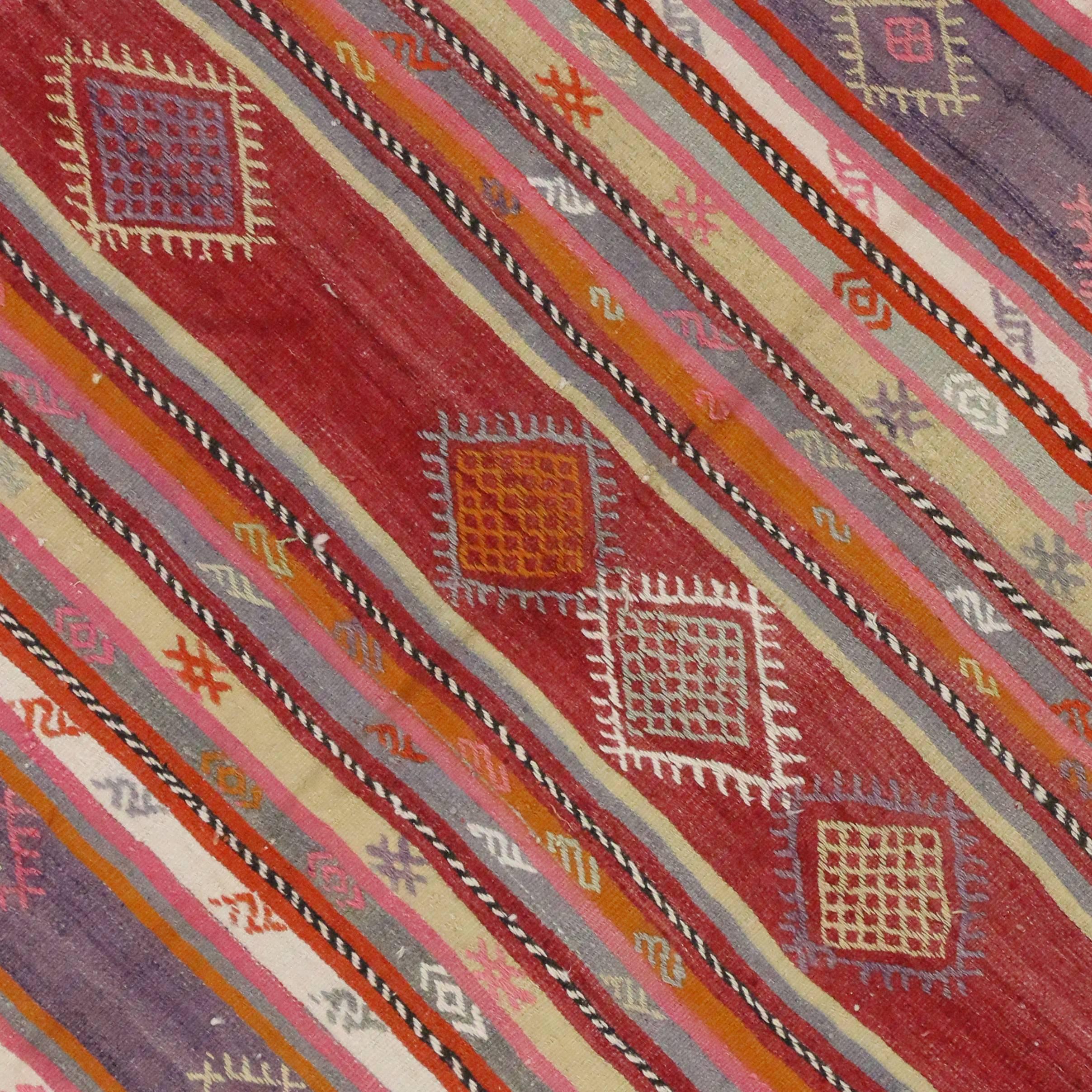 A colorful vintage handwoven vintage Turkish Kilim with Boho Chic style with stripes. This flat-weave Kilim rug features colorful stripes and Turkish tribal motifs. Rendered in pink, purple, red, orange and white. Among the multitude of designs,