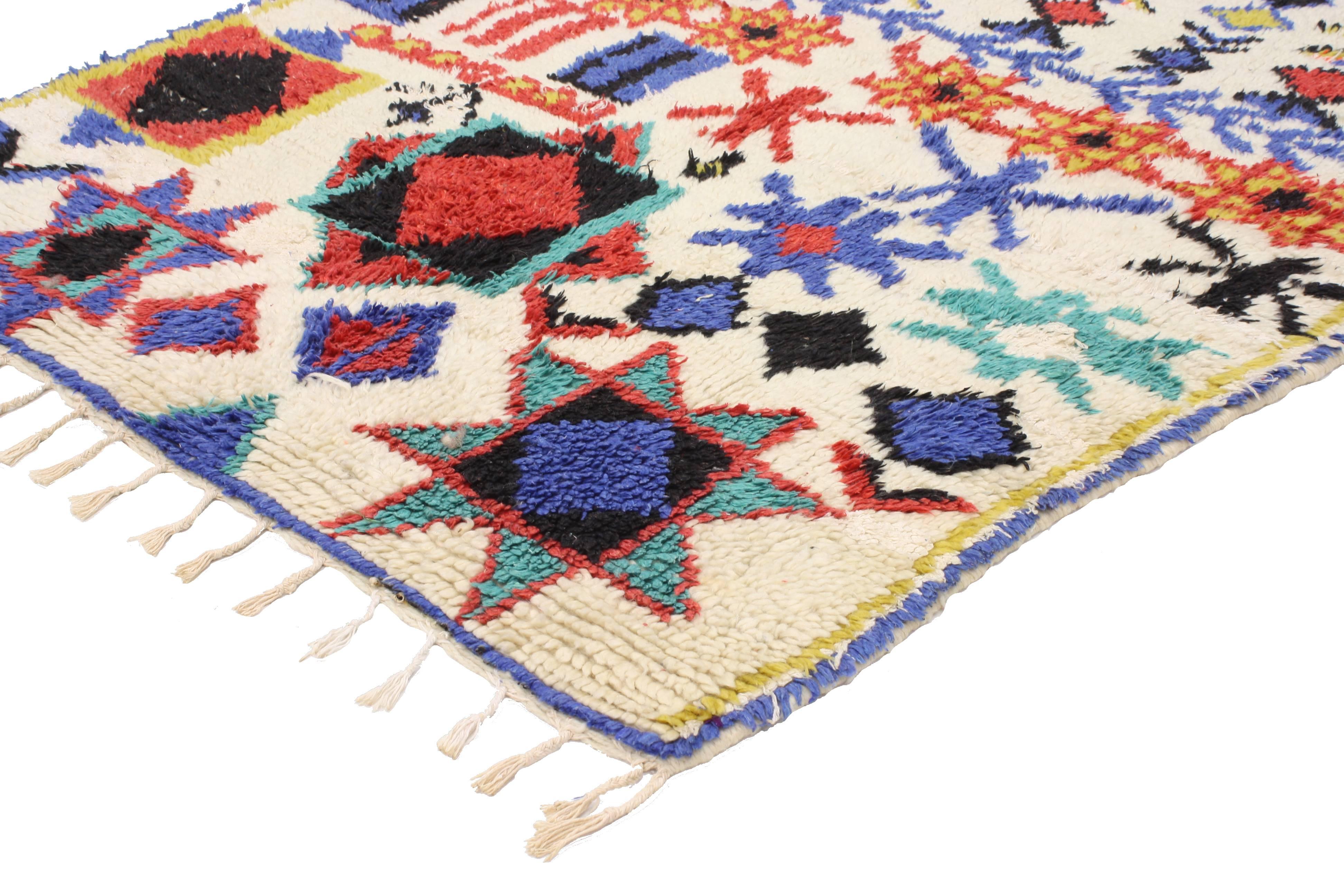 This vintage Berber Moroccan rug was made in Azilal in the High Atlas Mountains. Like typical Azilal rugs and carpets, this Moroccan rug features an ivory-white field with symbolic tribal motifs in vibrant colors. Rendered in ivory-white, blue, red,