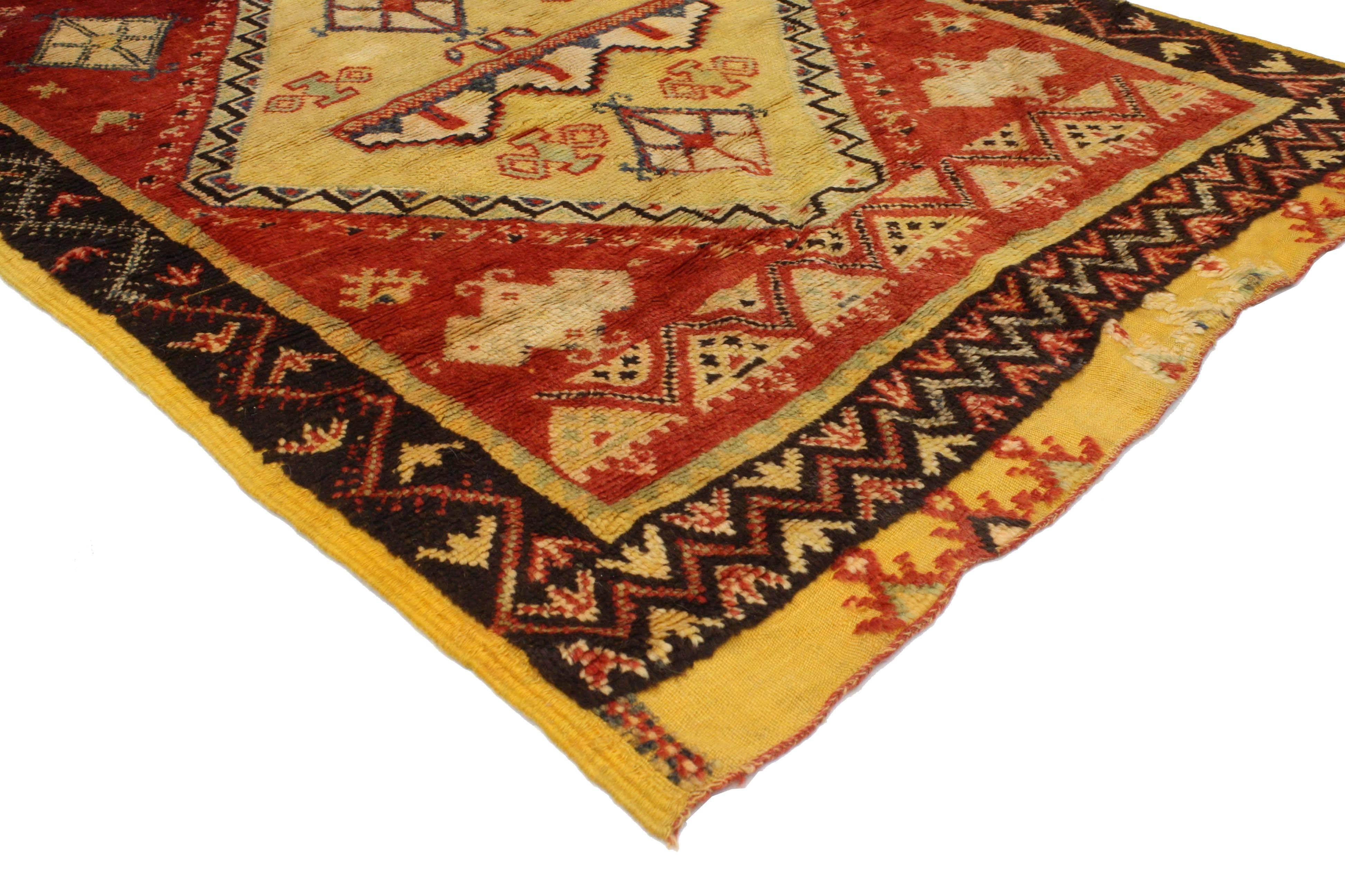 Impeccably woven from hand-knotted wool and displaying a modern tribal style, this vintage Berber Moroccan rug features three medallions surrounded by symbolic Berber motifs in an abrashed red field. Blending the graphic appeal and folk art warmth