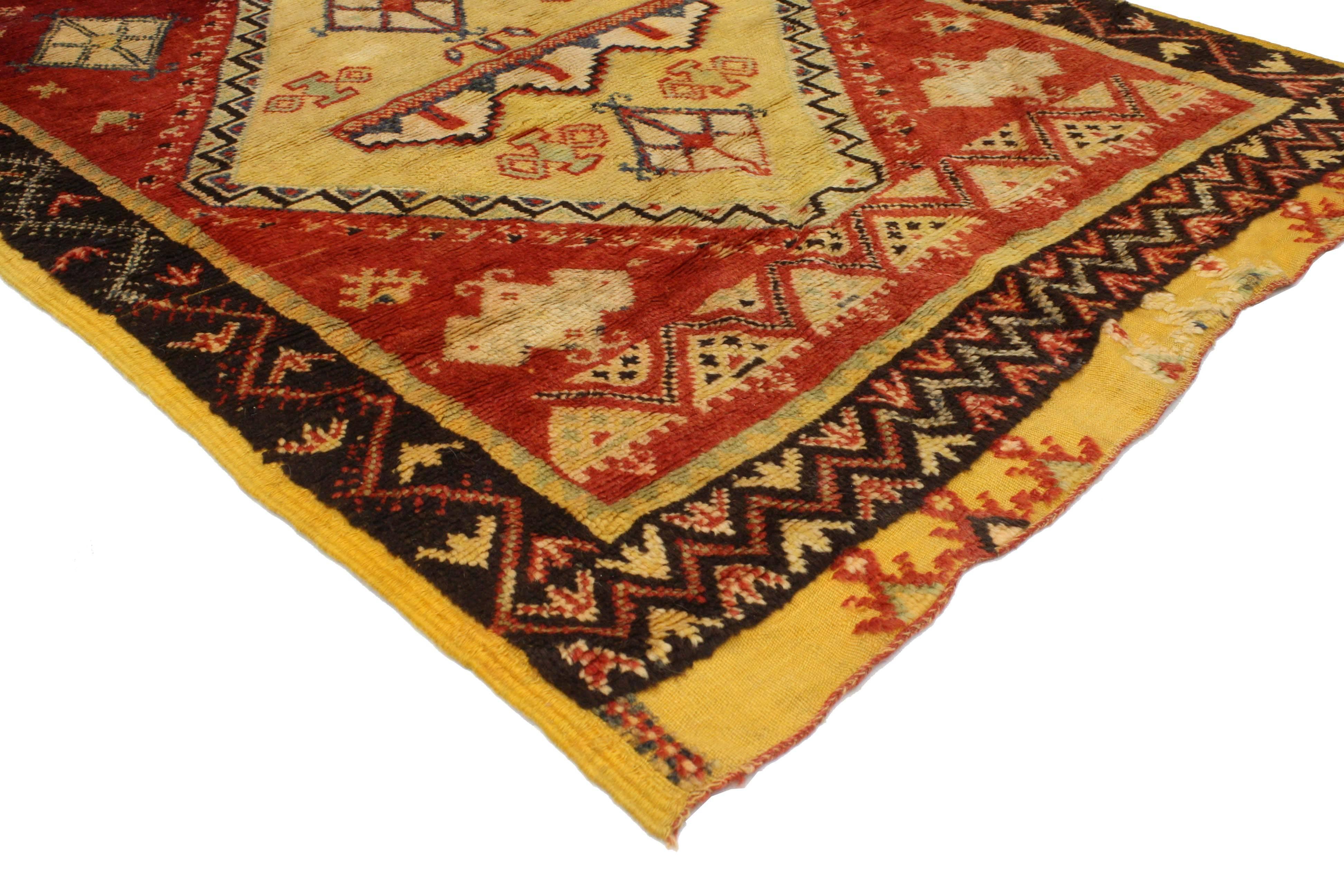 Impeccablement tissé en laine nouée à la main et affichant un style tribal moderne, ce tapis berbère marocain vintage présente trois médaillons entourés de motifs berbères symboliques dans un champ rouge abrasé. Alliant l'attrait graphique et la