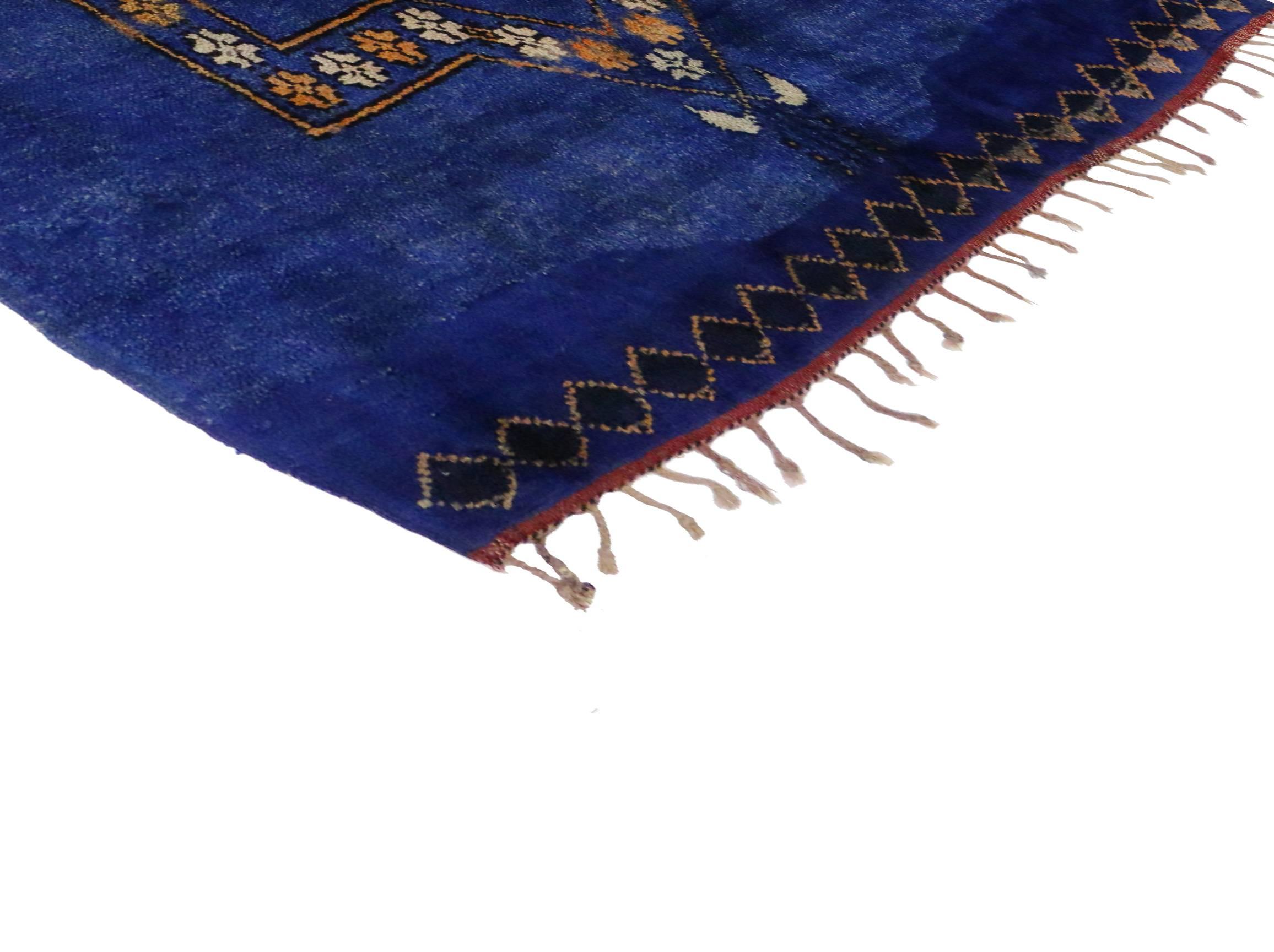 This vintage Berber Moroccan rug is saturated in cobalt blue highlighting a modern tribal design. An eight-pointed star medallion takes center stage and a small diamond border is found on the horizontal ends of the rug. Rendered in variegated shades