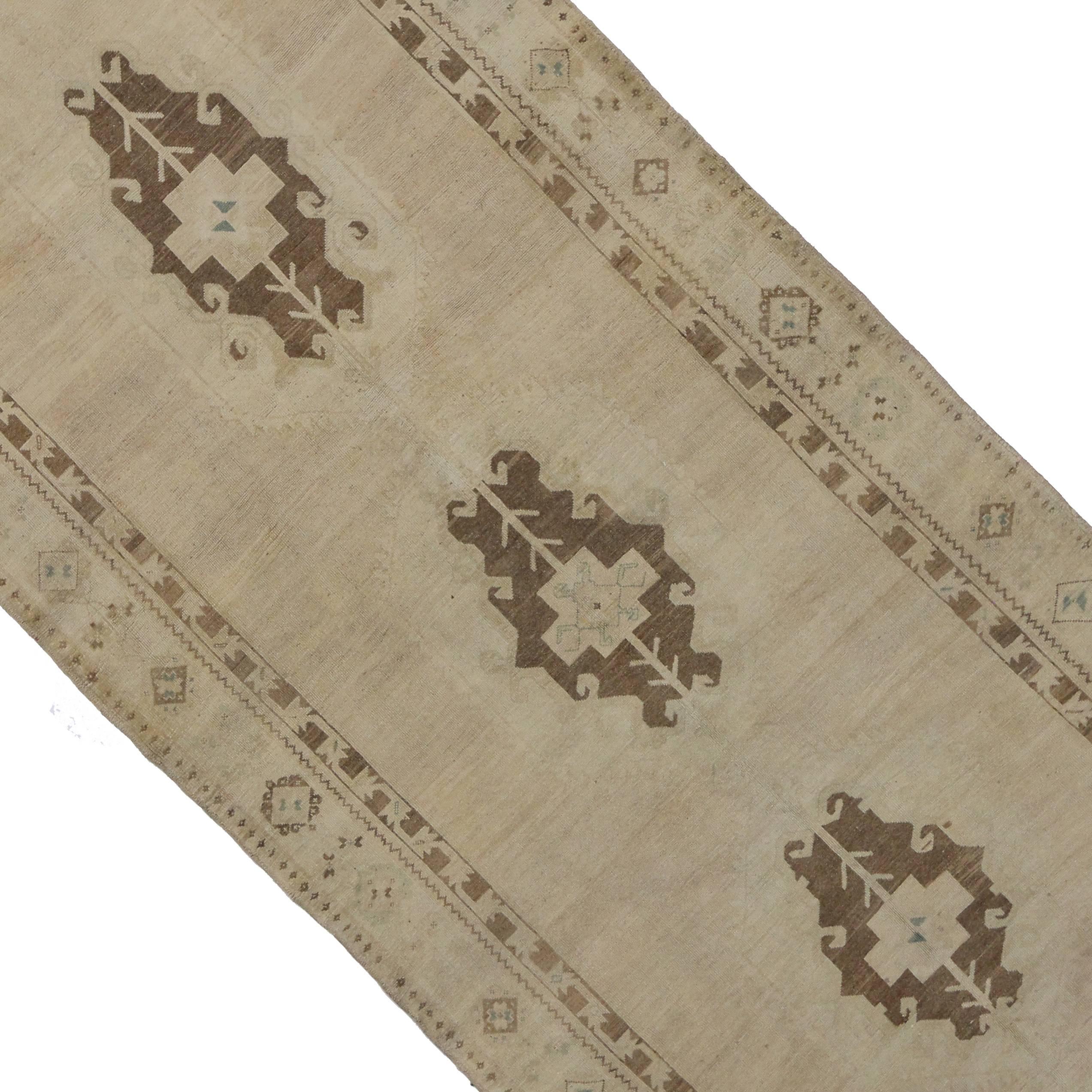 This stunning vintage Turkish Oushak gallery carpet runner bears a remarkable air of chic sophistication. A beautiful display of finely fashioned elegant medallions are delicately weaved as if they are floating in the washed-out colored field. The