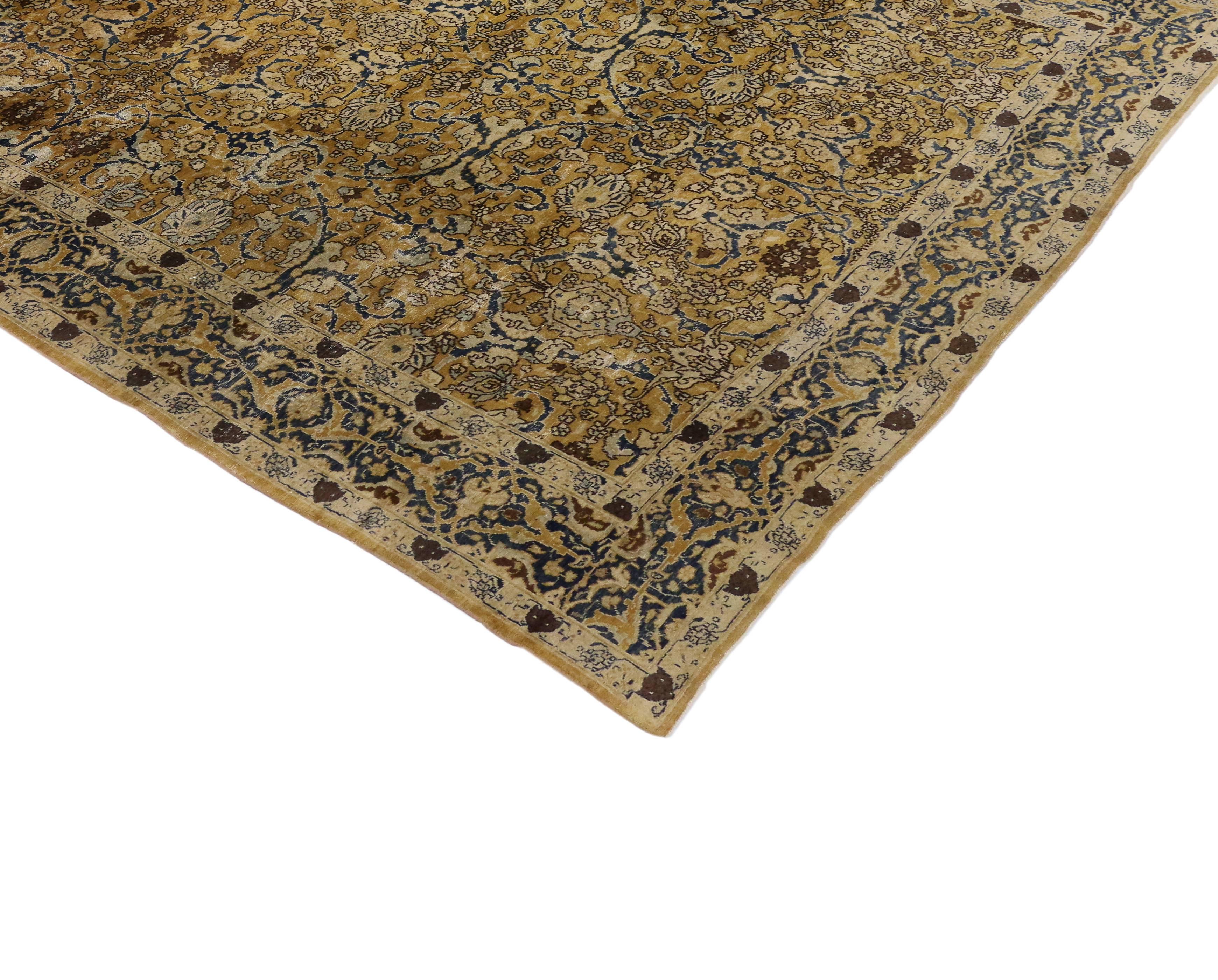 Saturé d'une extraordinaire palette d'or et de bleus, ce tapis persan Kirman ancien présente un exquis motif sur toute sa surface. Les vignes arabesques serpentent à travers un pot-pourri de fleurs exquisément composées, créant une cadence