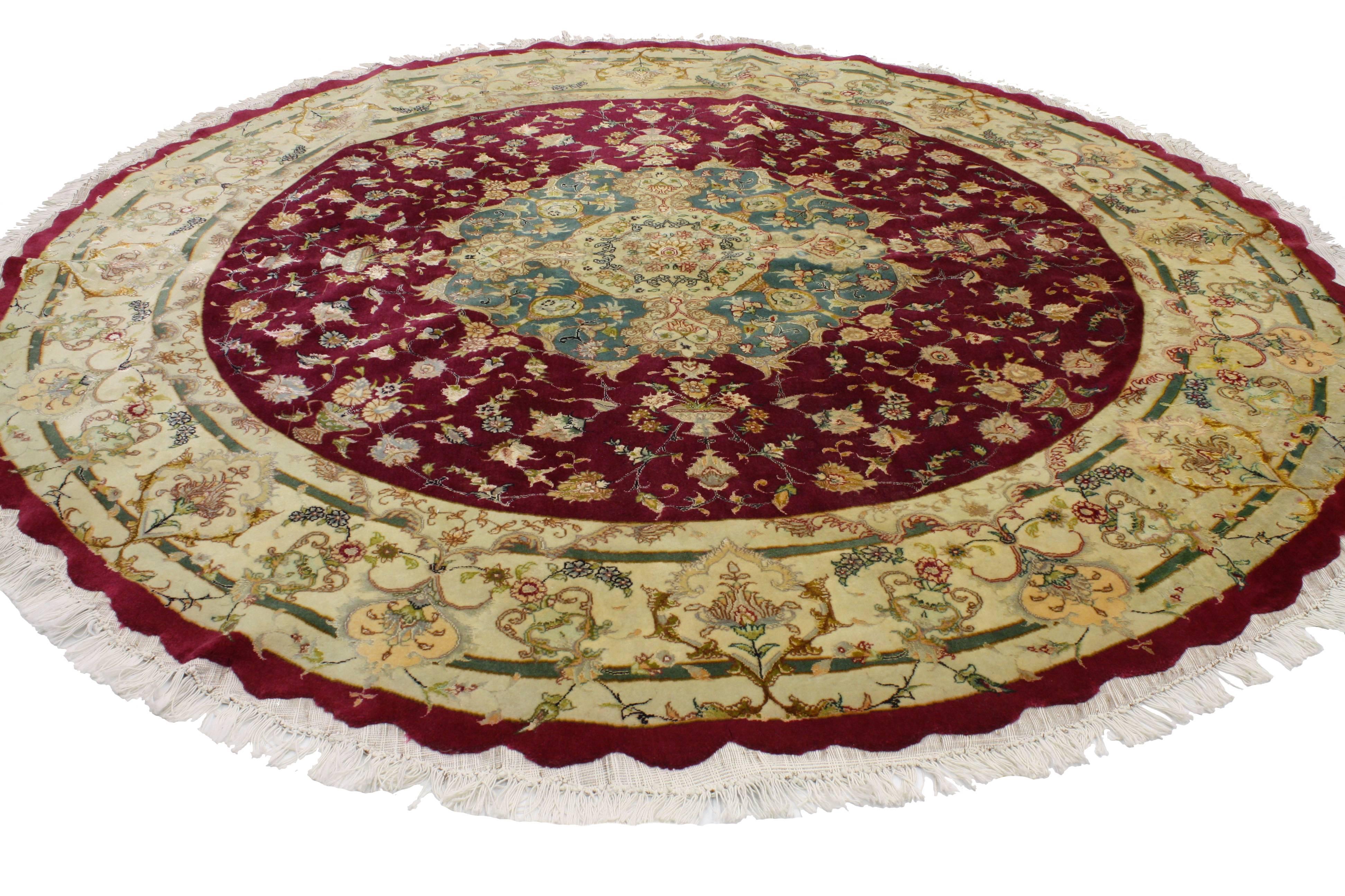 Timeless and refined, this round Persian Tabriz rug features traditional style. Taking center stage is an ornate medallion floating in a burgundy field. The medallion is surround by all-over florals abundantly flowing from Persian vases. A