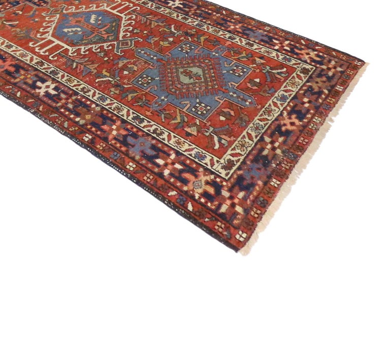 Antique hand-knotted wool Persian Heriz runner featuring alternating medallions with an all-over geometric design on an orange-red field. Surrounded by a blue border with tribal motifs. Rendered a refined color palette of orange-red, navy, blue,