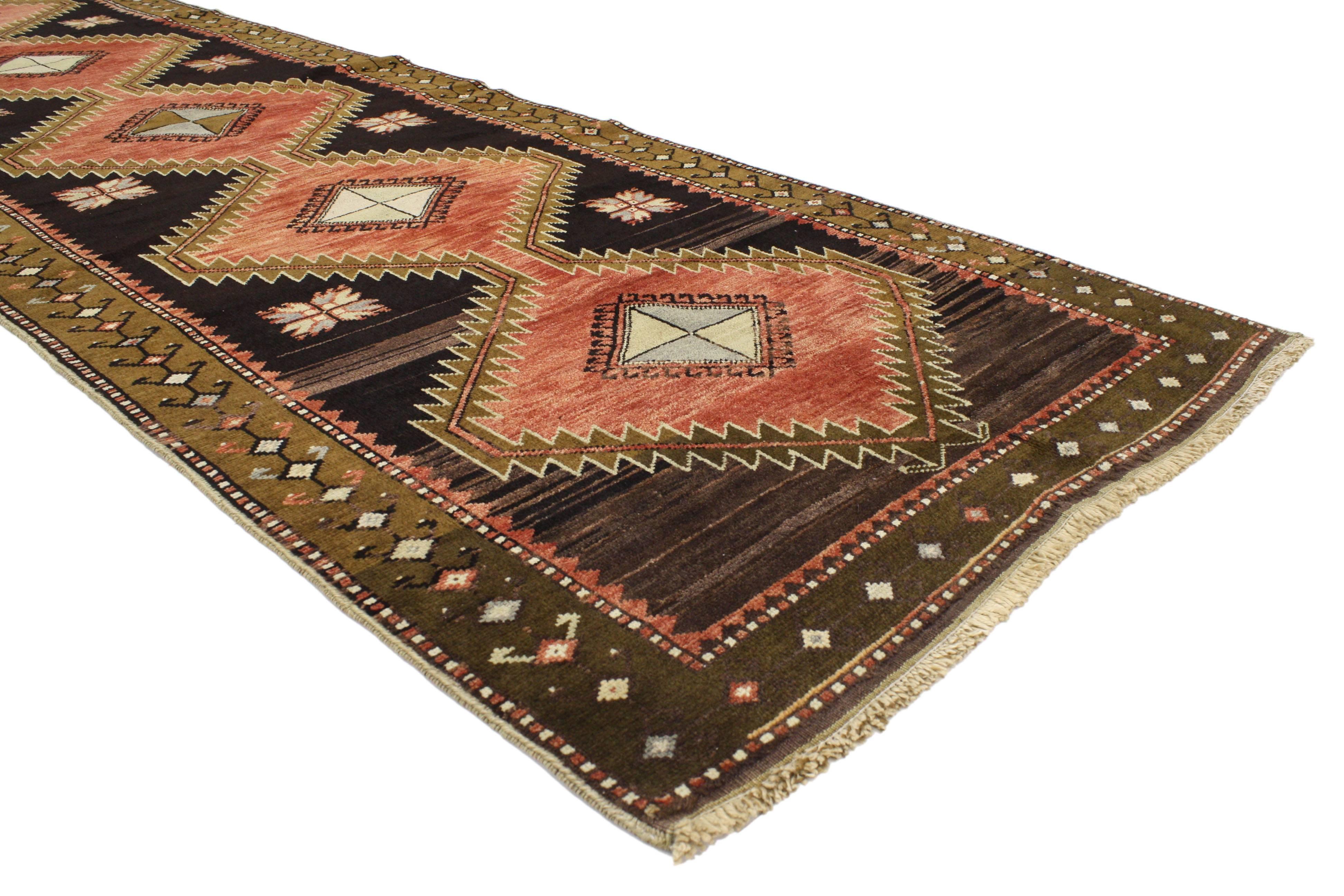 This hand-knotted wool vintage Turkish Oushak runner with Modern Tribal Style features two large hexagonal medallions with Turkish motifs in an abrashed red field surrounded by a small geometric border. Rendered in variegated shades of red, dark