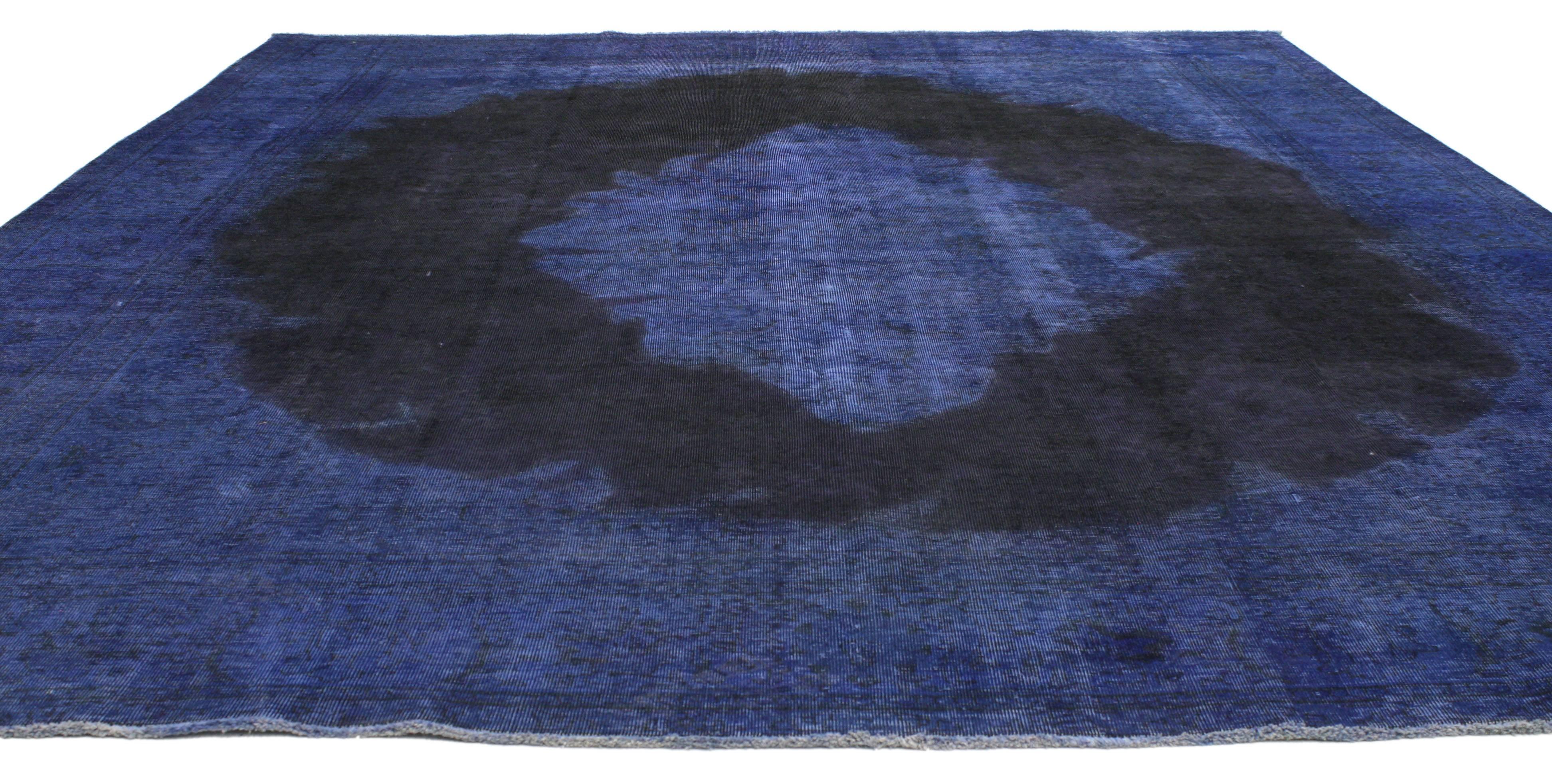 This beautifully composed overdyed blue vintage Persian gallery rug features a center medallion in an open navy blue field surrounded by a complementary border highlighting its modern Industrial style. Deeply saturated with variegated shades of blue