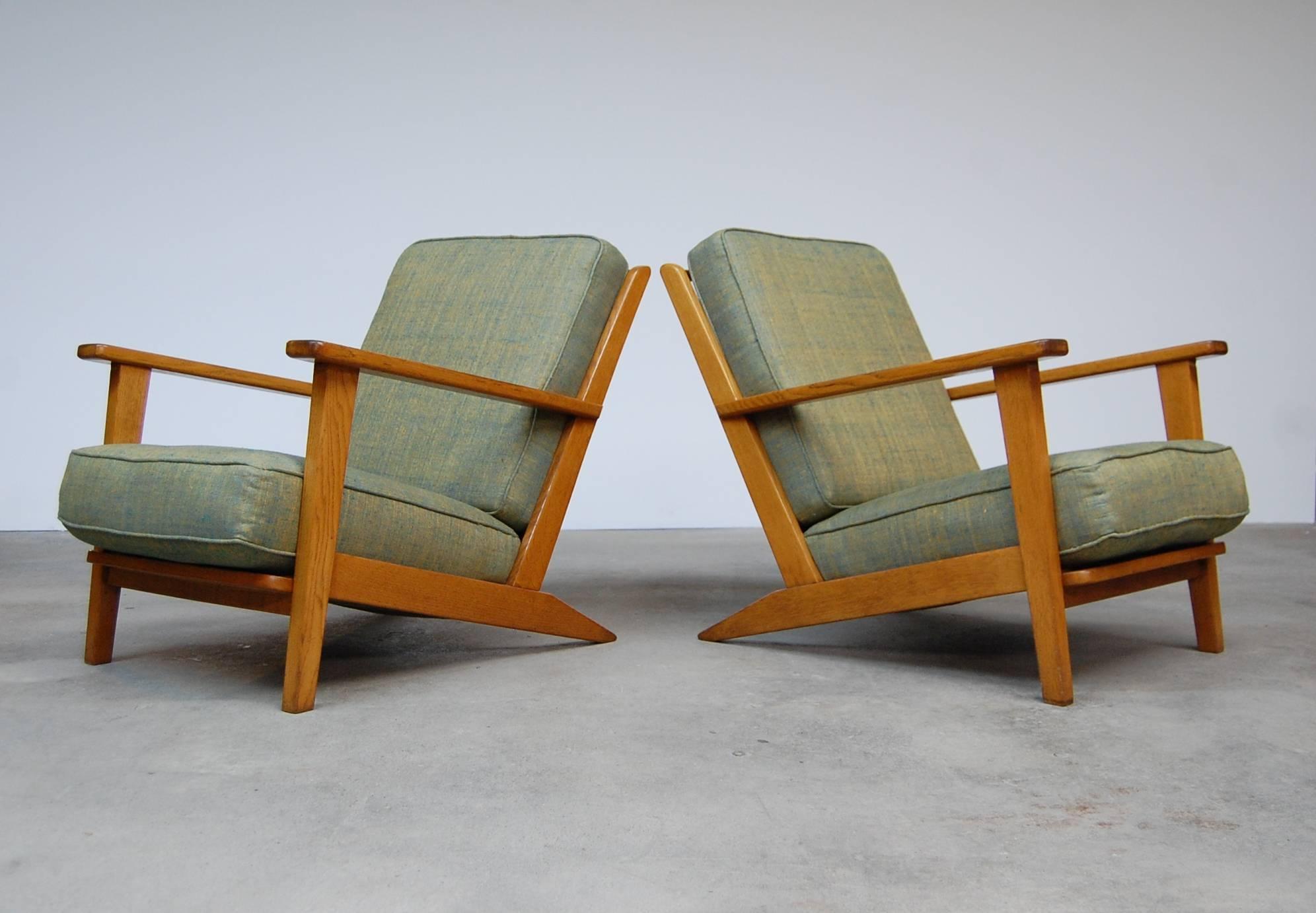 Pair of low lounge chairs in oak from France, circa 1950. Chairs have loose cushions and have been reupholstered in raw silk. Coil springs have been wrapped in silk as well, just as they originally were. Seat cushions have internal springs. Very