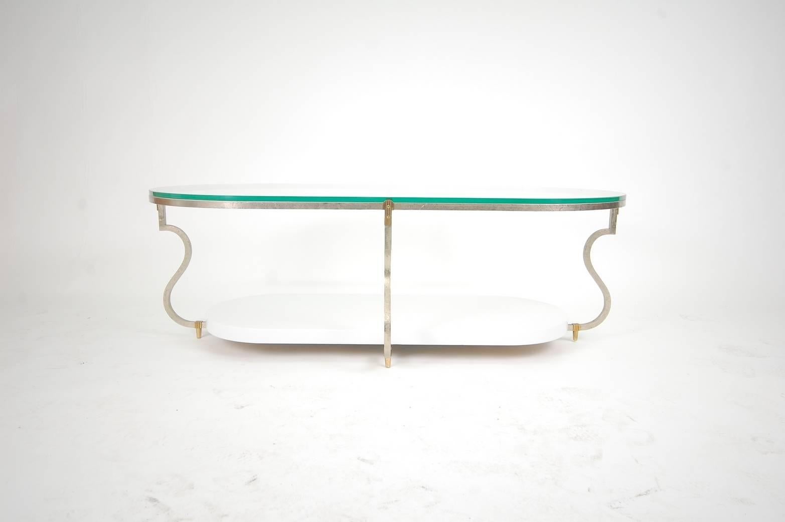 Elegant obround cocktail table designed by Tommi Parzinger for Parzinger Originals, circa 1966. Table consists of a hand-wrought, silvered steel frame, with handmade, solid brass hardware, a white lacquered lower shelf and a glass top.

We offer