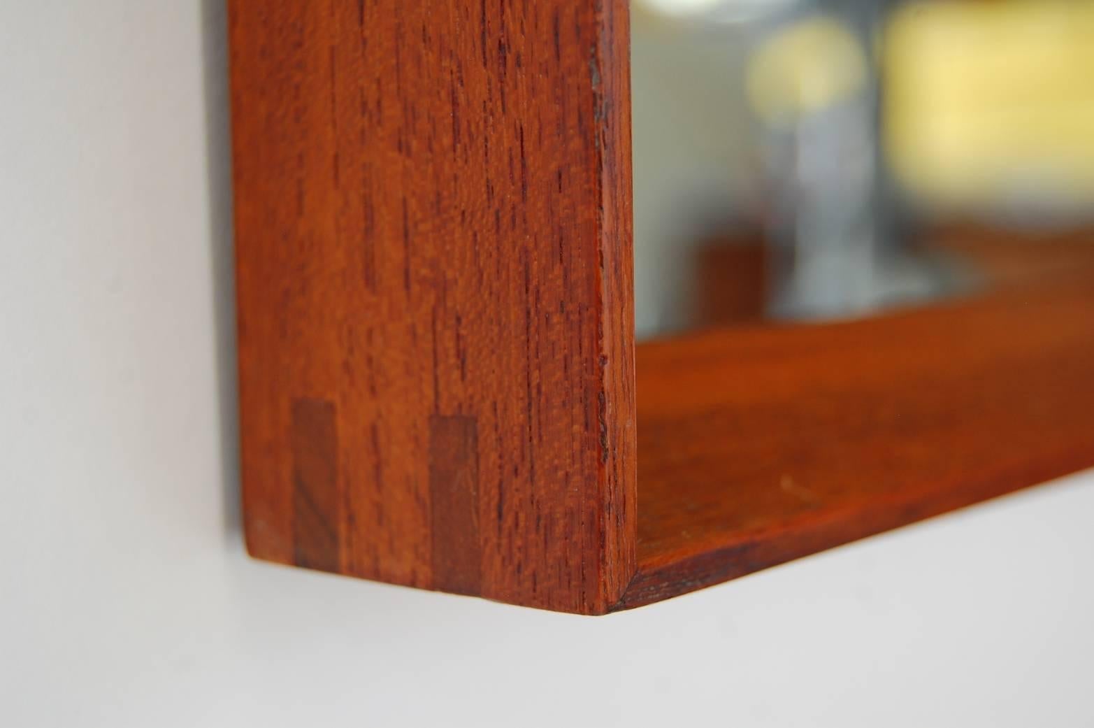 Wall shelf and mirror in teak by Ludvig Pontoppidan, Copenhagen, Denmark, circa 1959. Mirror is framed in teak. Shelf is in teak as well, and has a beautifully turned teak knob. Face of shelf unit folds down/out to reveal a small storage