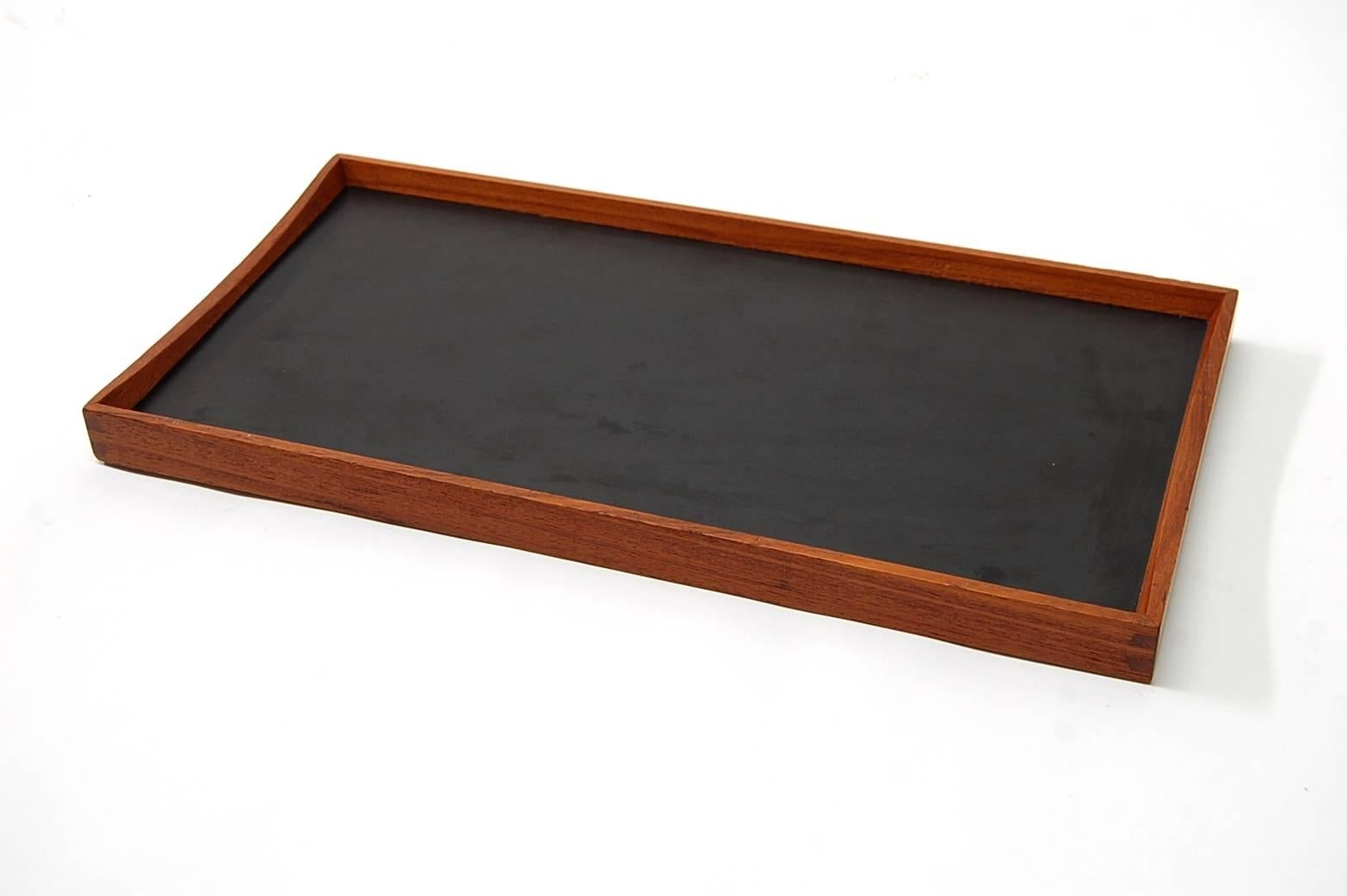 Finn Juhl designed this useful tray in 1957 for Torben Ørskov, of Denmark. Their frames are beautifully joined teak, while their working surfaces are in melamine, one face is a vibrant red, the other (reversibly) black. The profile of the teak frame